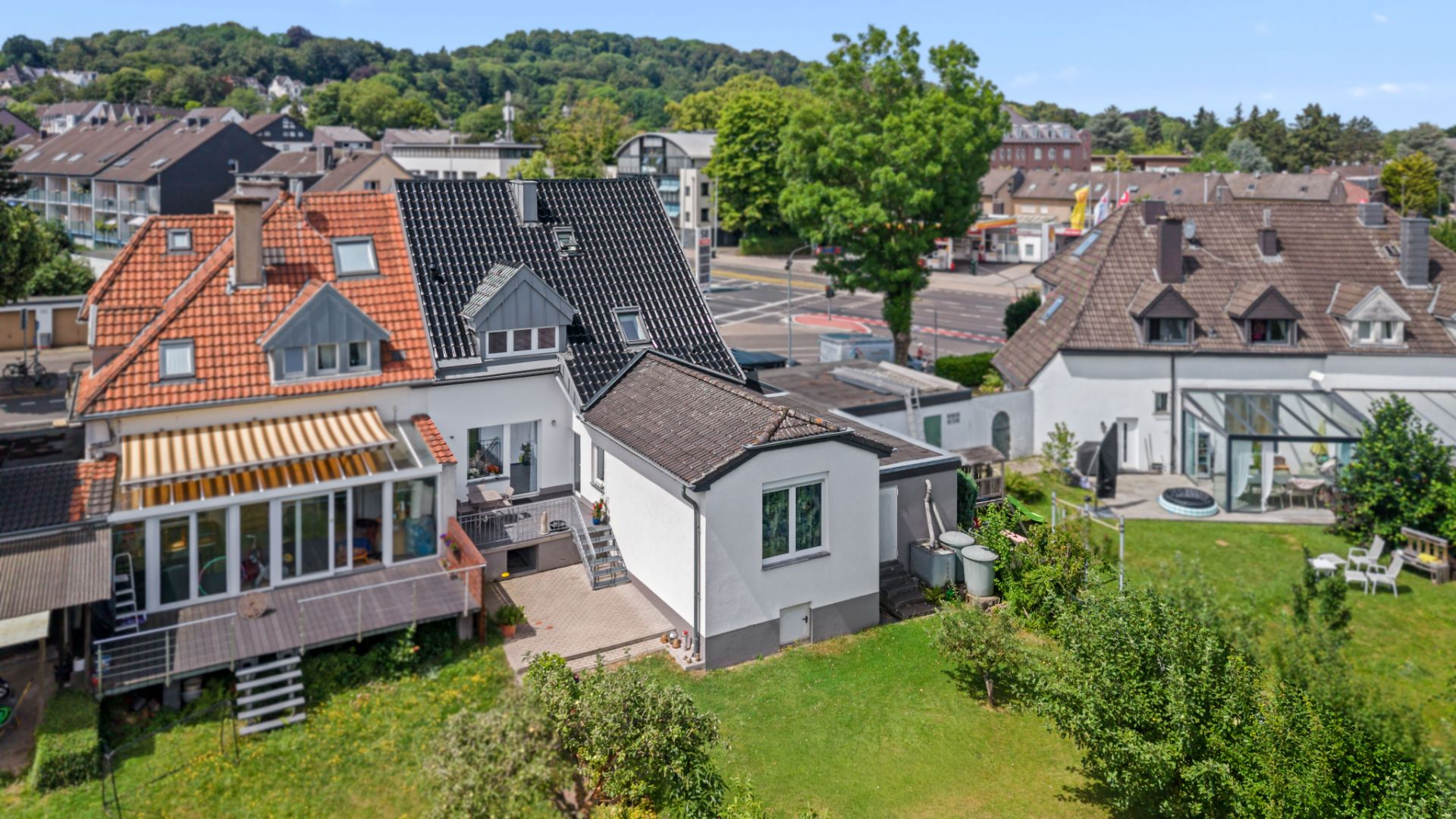 Zwei angrenzende Wohnhäuser mit Terrassen und großem Garten, im Hintergrund weitere Häuser und Bäume.