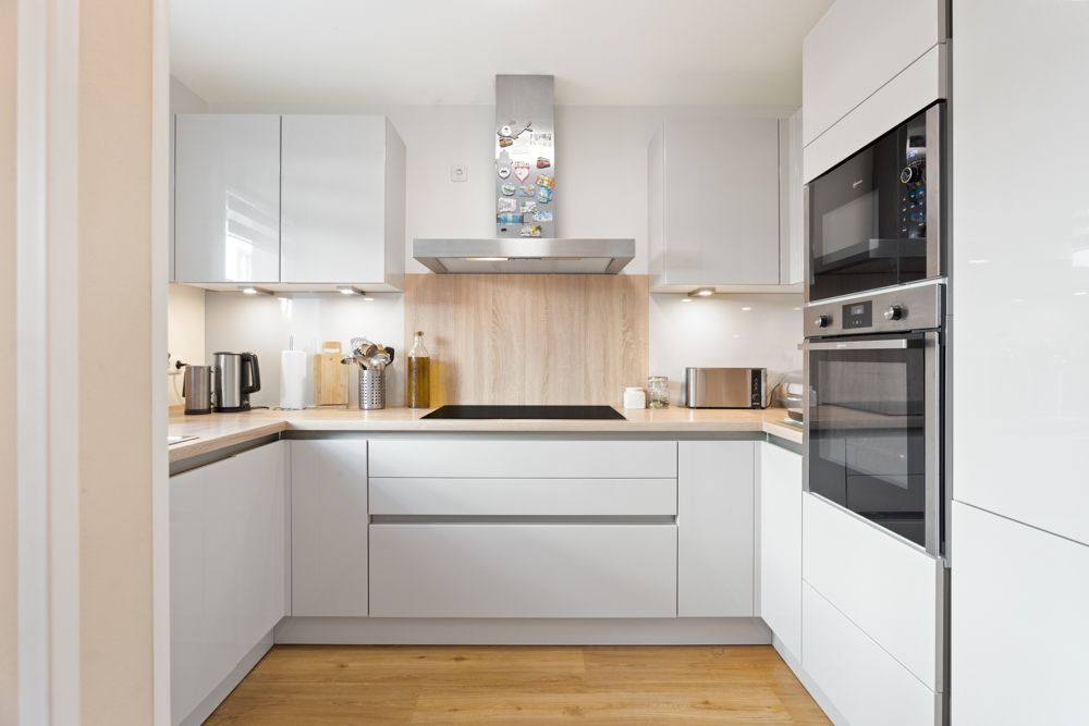 Moderne Einbauküche mit weißen Schränken, Kochfeld, Backofen und Holzarbeitsplatte.