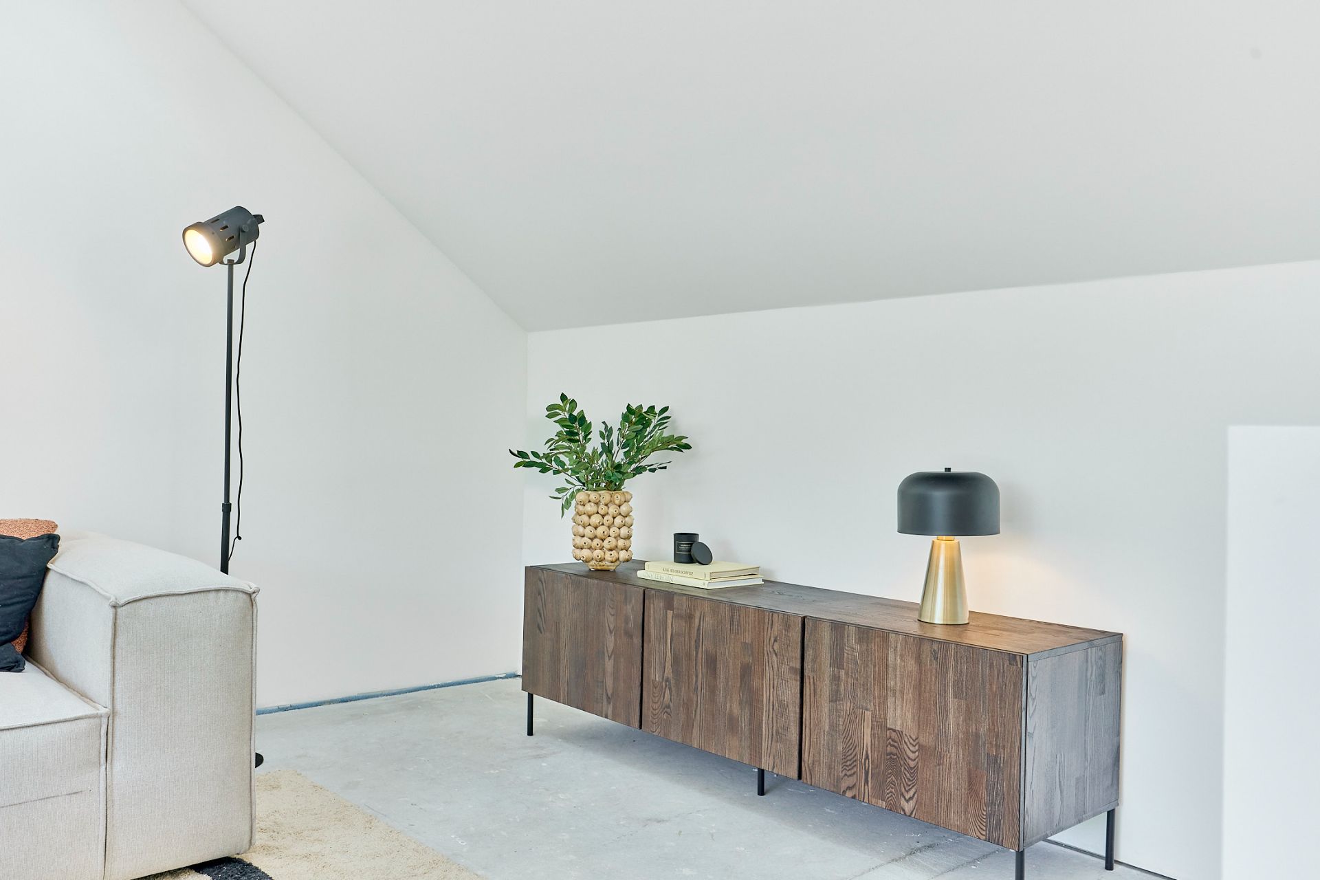 Wohnzimmer mit hellgrauem Sofa, Stehlampe und Sideboard mit Deko und Tischlampe.