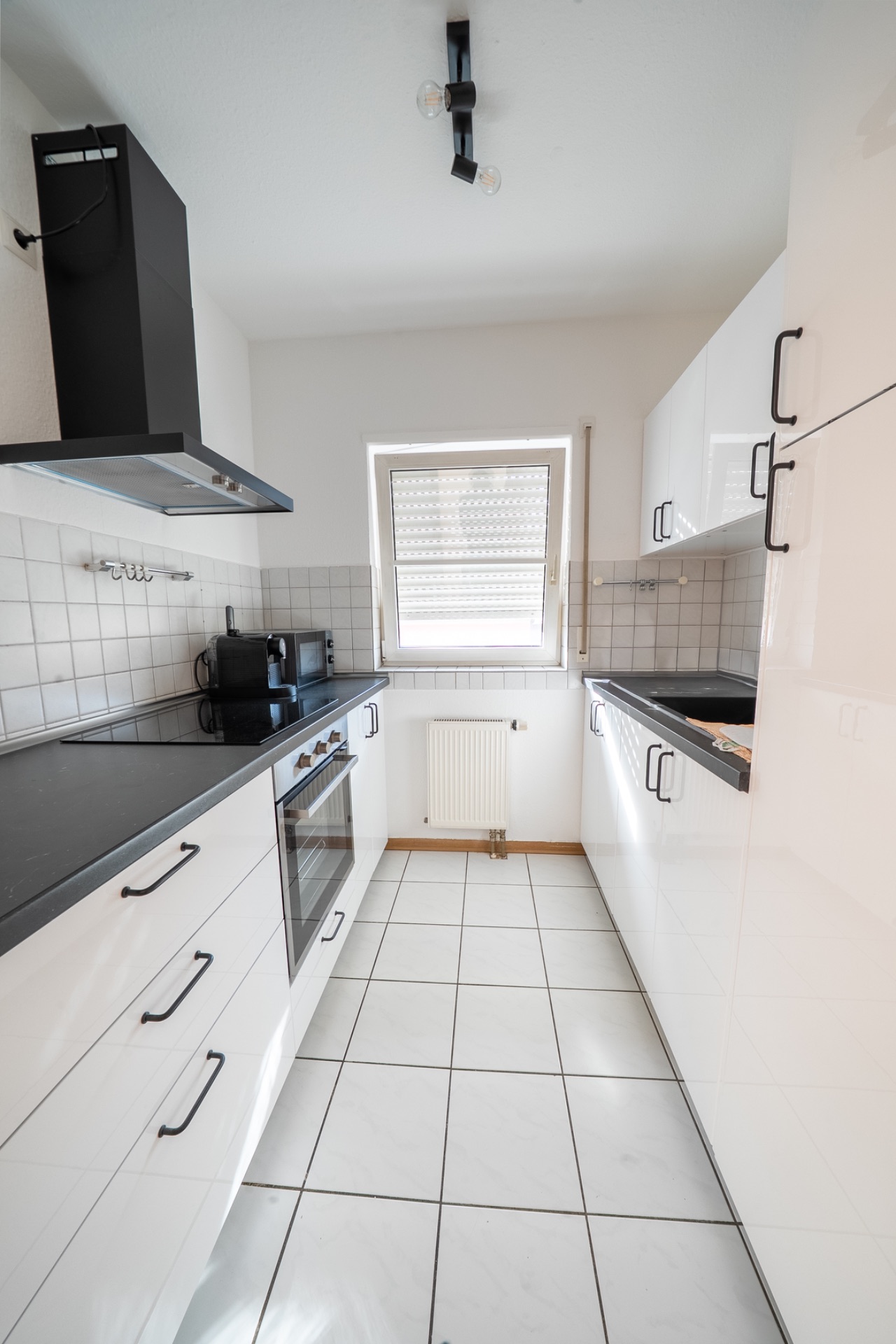 Moderne weiße Einbauküche mit Fenster, Herd, Backofen und Hängeschränken.