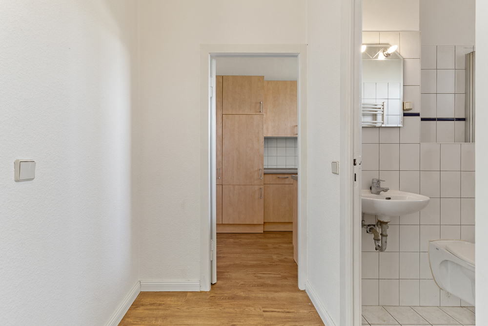Flur mit Blick auf Küche mit Holzfronten und Badezimmer mit weißem Waschbecken und Fliesen.
