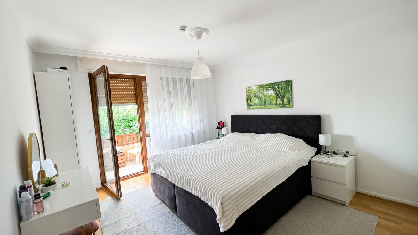 Helles Schlafzimmer mit großem Bett, Nachttischen, Kommode und Zugang zu einem Balkon.
