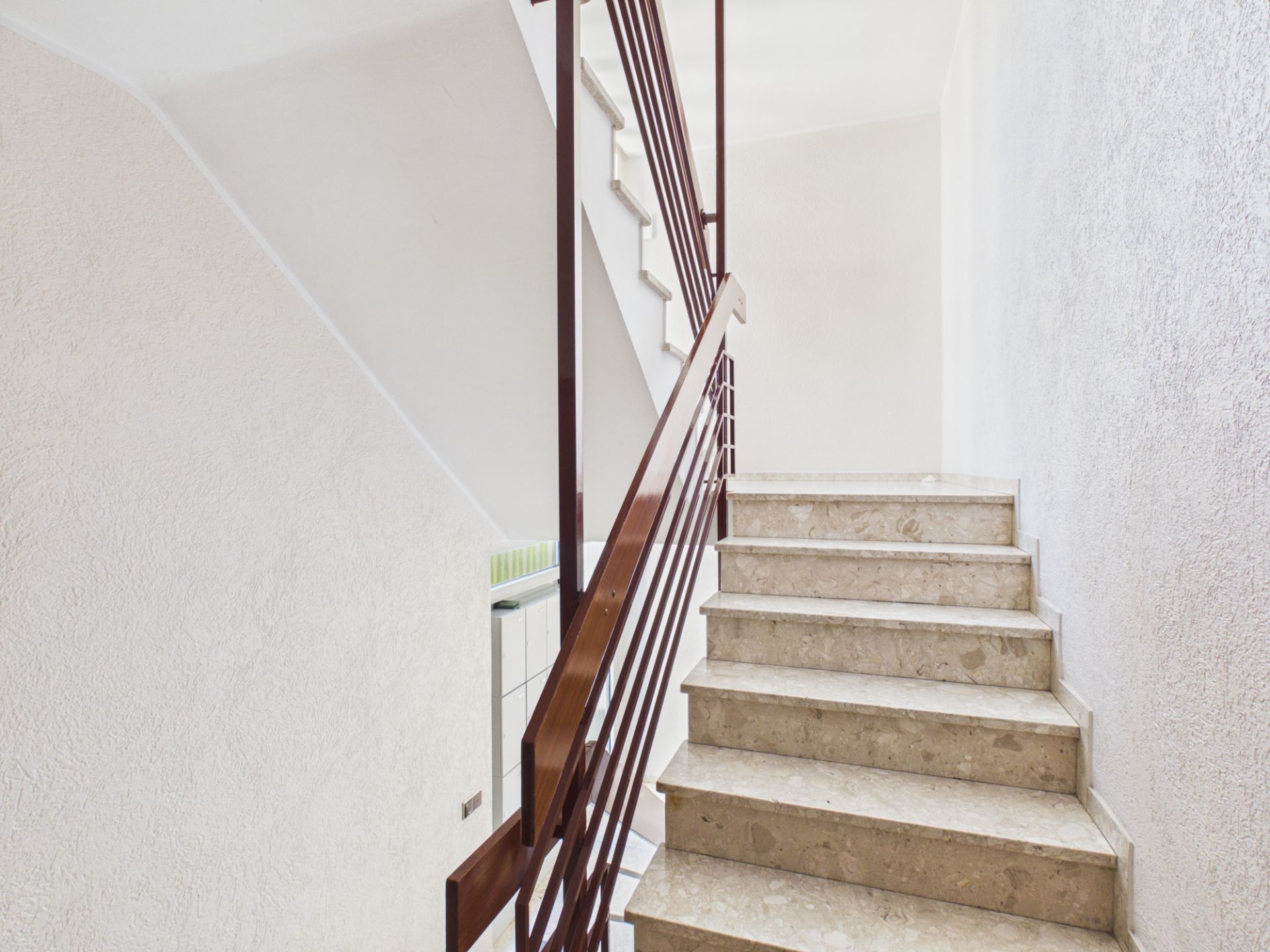 Helle Treppe mit beigem Marmor und braunem Geländer in einem Wohnhaus.