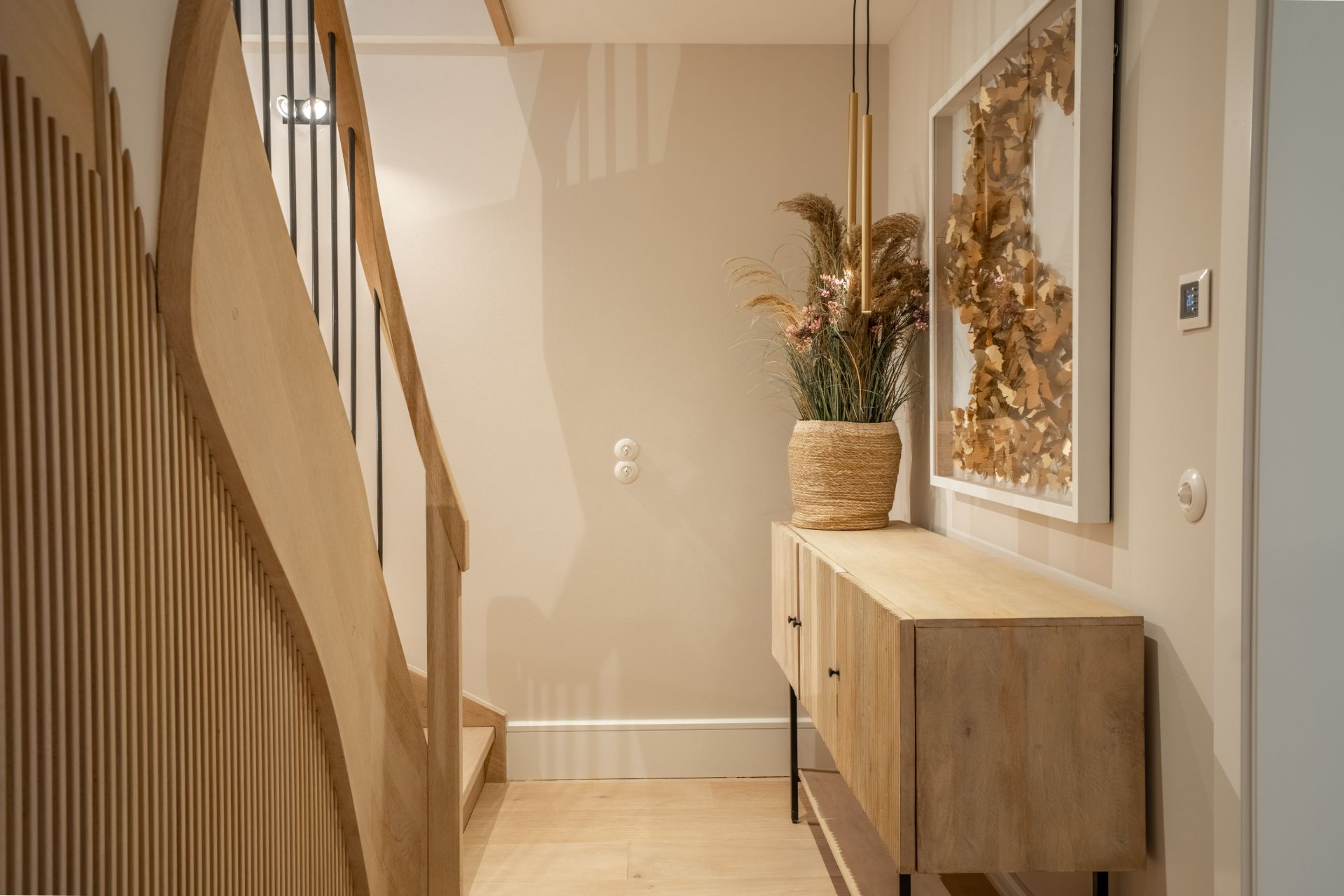 Heller Flur mit Holztreppe, Sideboard, Pflanze und gerahmtem Bild an der Wand.