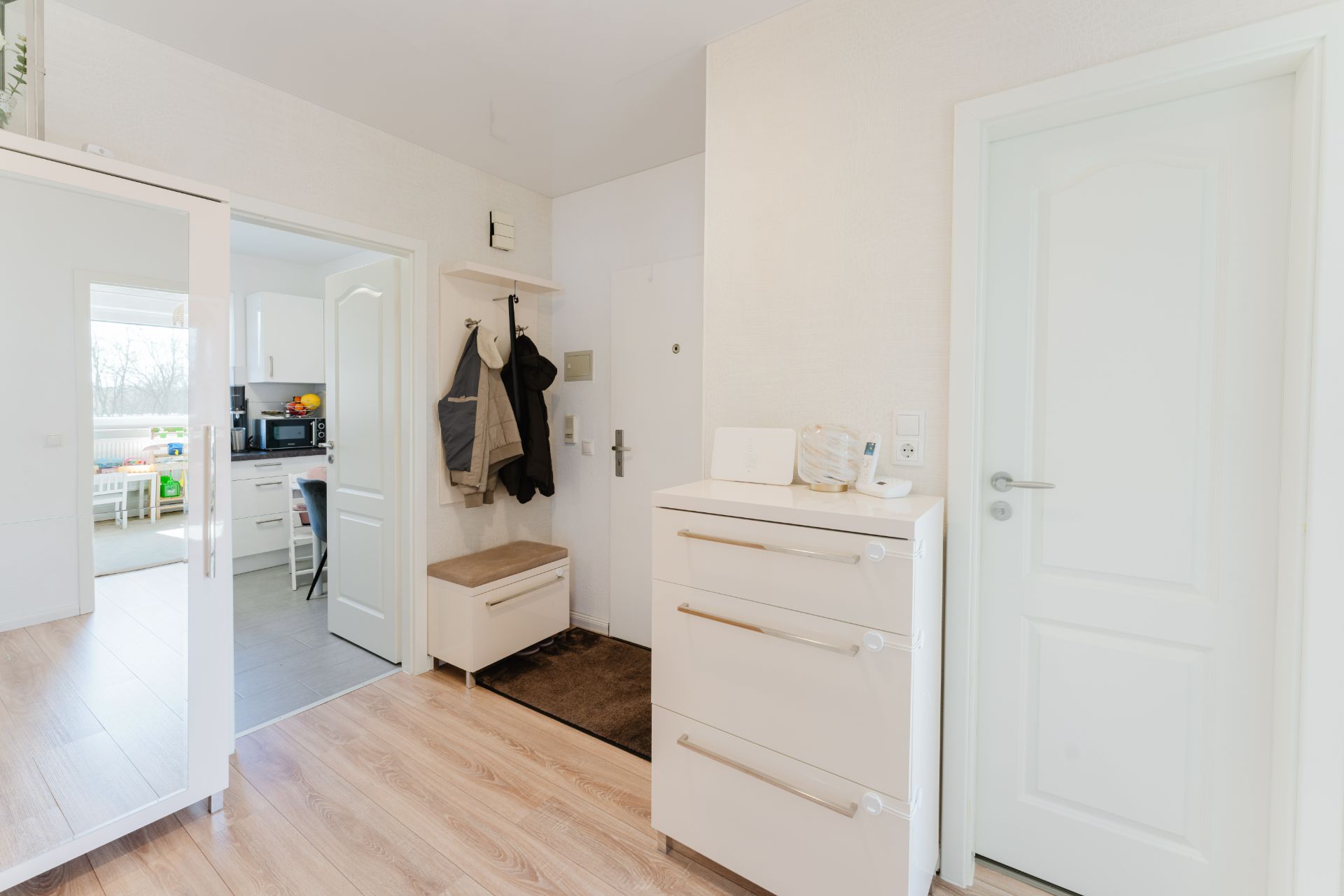 Heller Eingangsbereich mit Garderobe, Kommode und Blick in Küche und weiteres Zimmer.