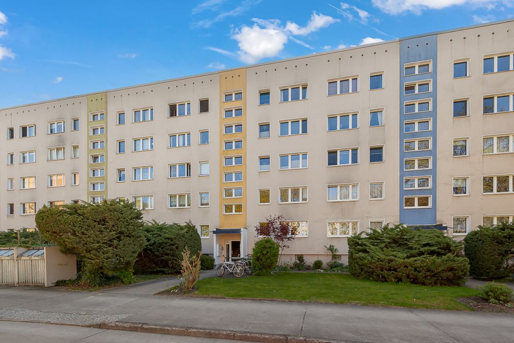 Mehrfamilienhaus mit vier Etagen, mehreren Fenstern und gepflegtem Vorgarten.
