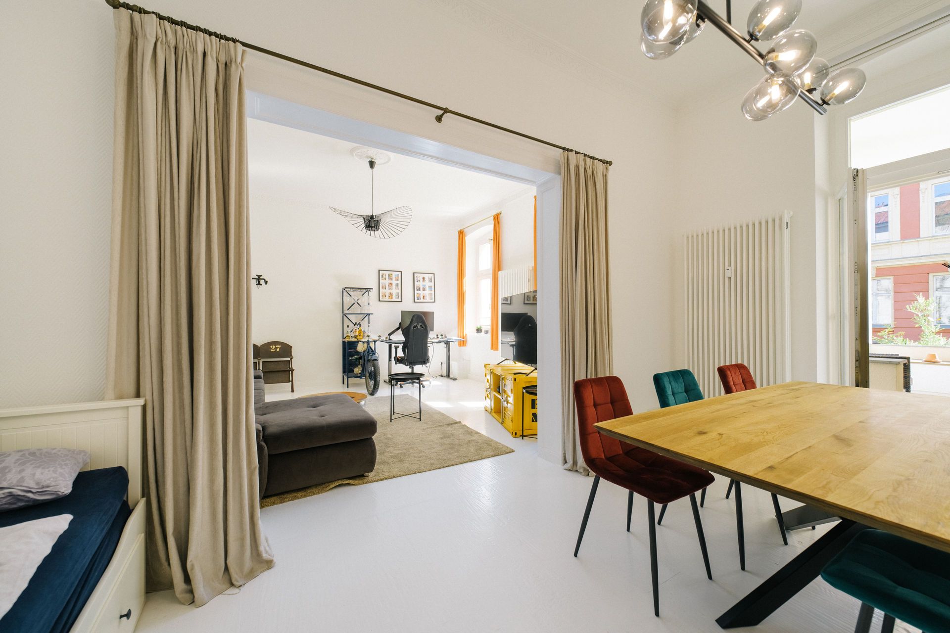 Helles Wohnzimmer mit Essbereich, Holztisch, bunten Stühlen und Sofa, daneben großer Fensterausblick.