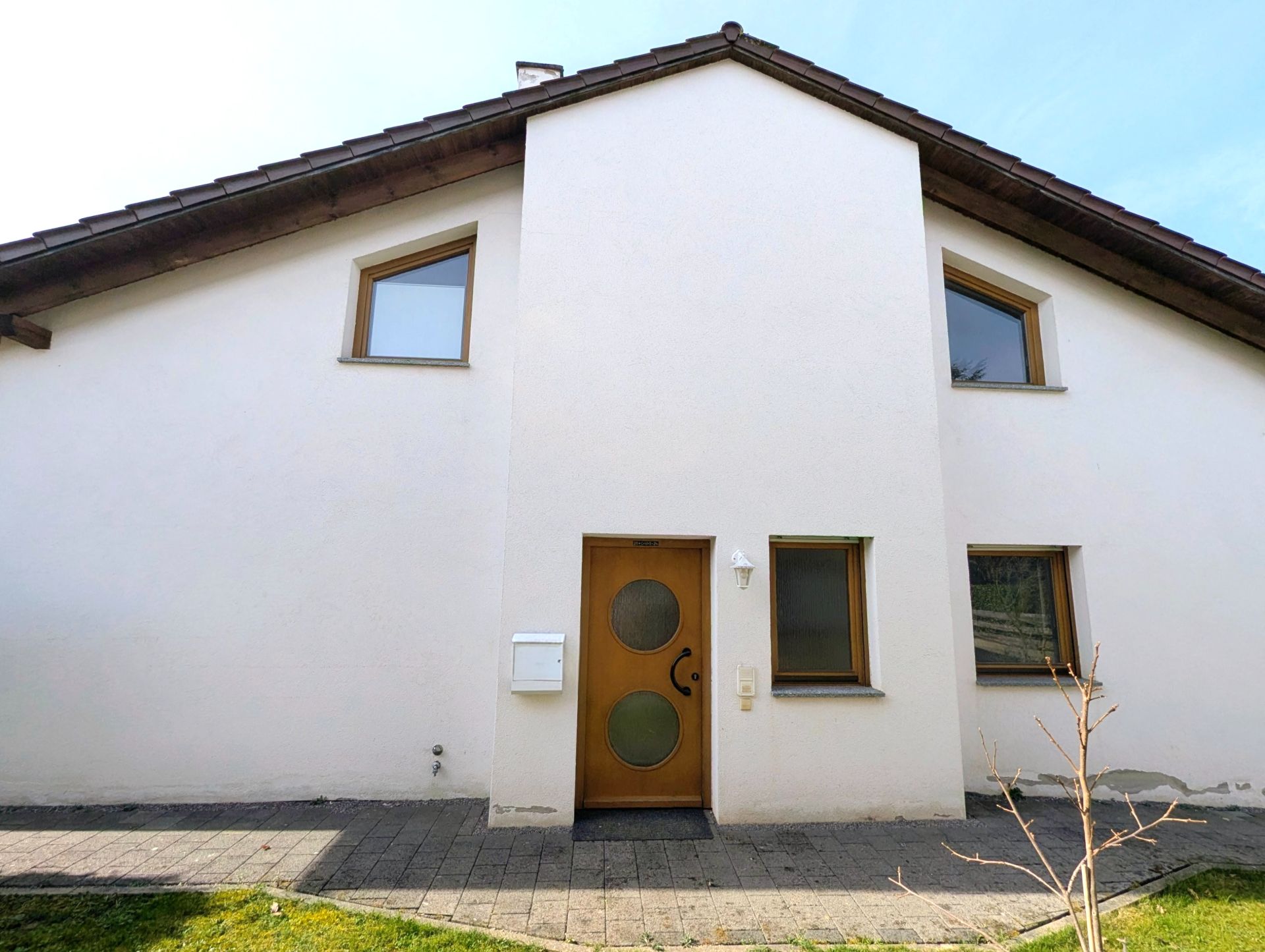 Weiße Hausfassade mit Holztür, drei Fenstern und schrägem Dach.