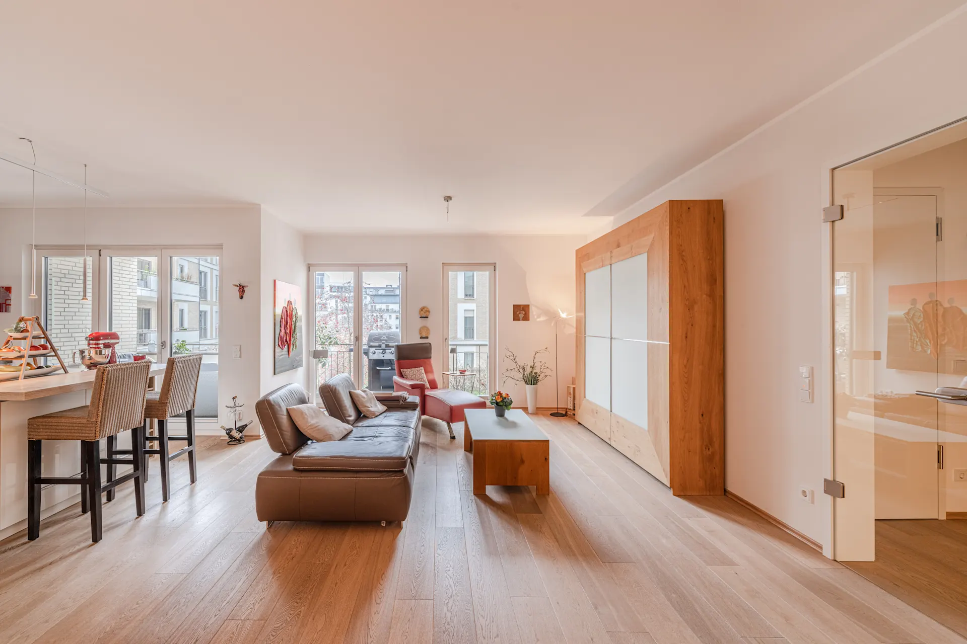 Modernes Wohnzimmer mit braunem Sofa, Esstresen, großen Fenstern und Holzboden.