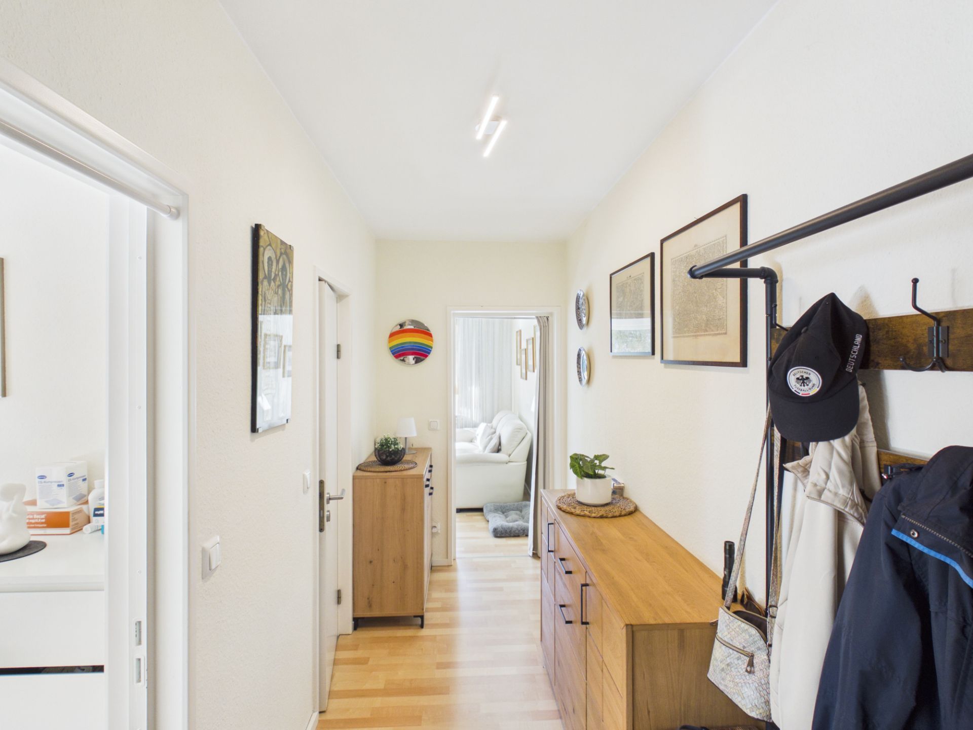 Heller Flur mit Holzkommode, Garderobe, Bildern an der Wand und Blick ins Wohnzimmer.