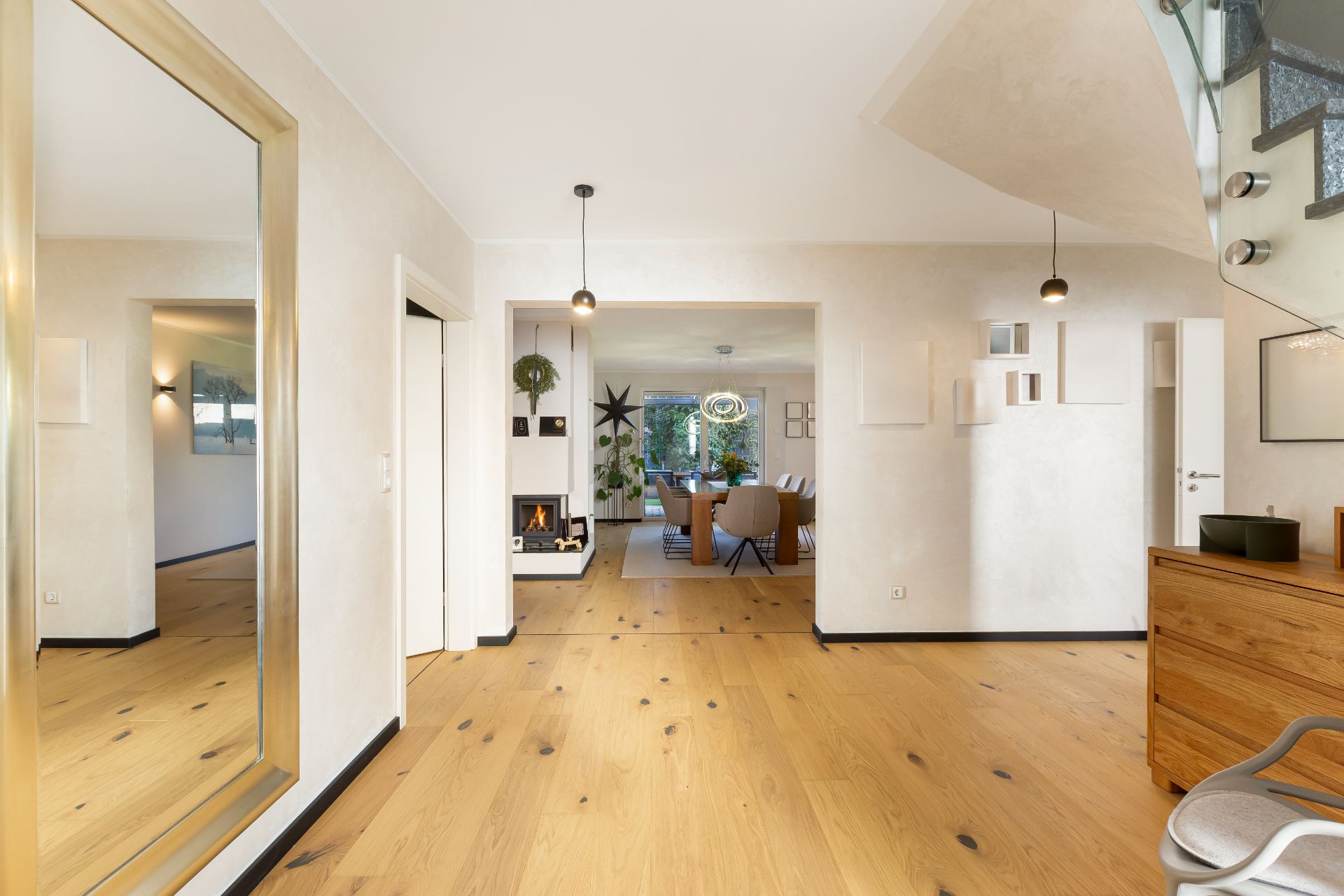 Heller Flur mit Holzfußboden, großem Spiegel und Blick ins Wohnzimmer mit Kamin.