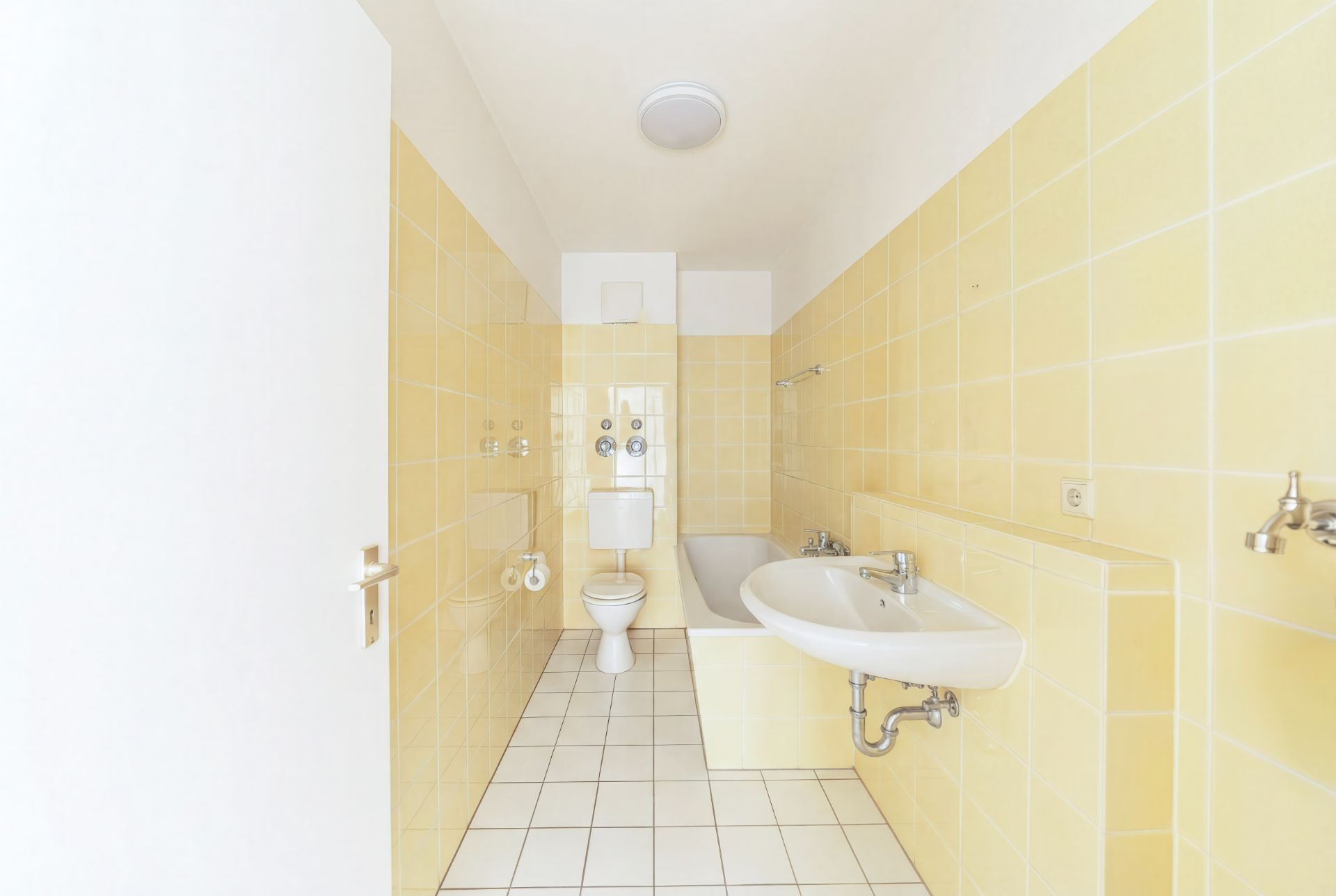Helles Badezimmer mit gelben Fliesen, Waschbecken, Toilette und Badewanne.