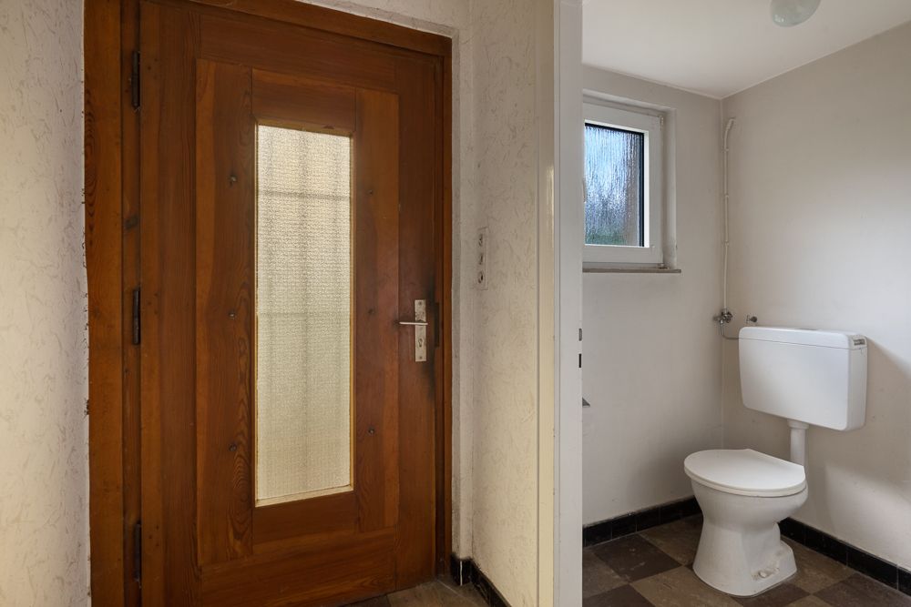 Holztür neben einem kleinen Badezimmer mit Toilette und Fenster.