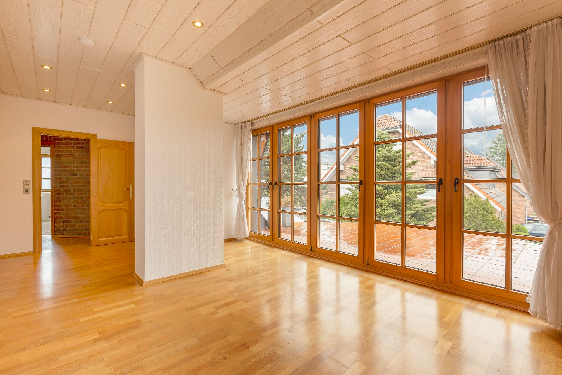Helles Wohnzimmer mit Holzfußboden und großen bodentiefen Fenstern zur Terrasse.