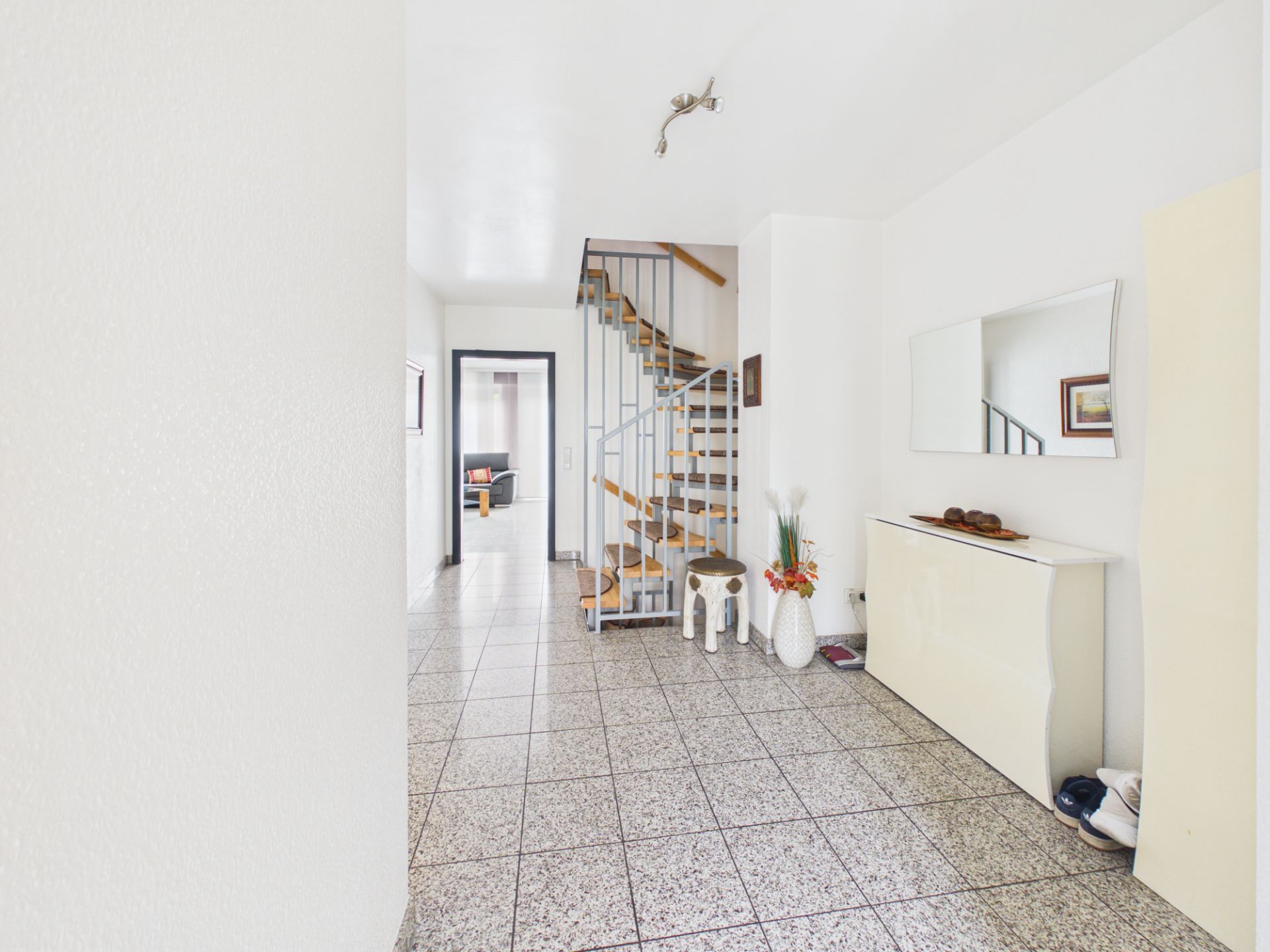Heller Flur mit Treppe, Spiegel, Sideboard und Fliesenboden.