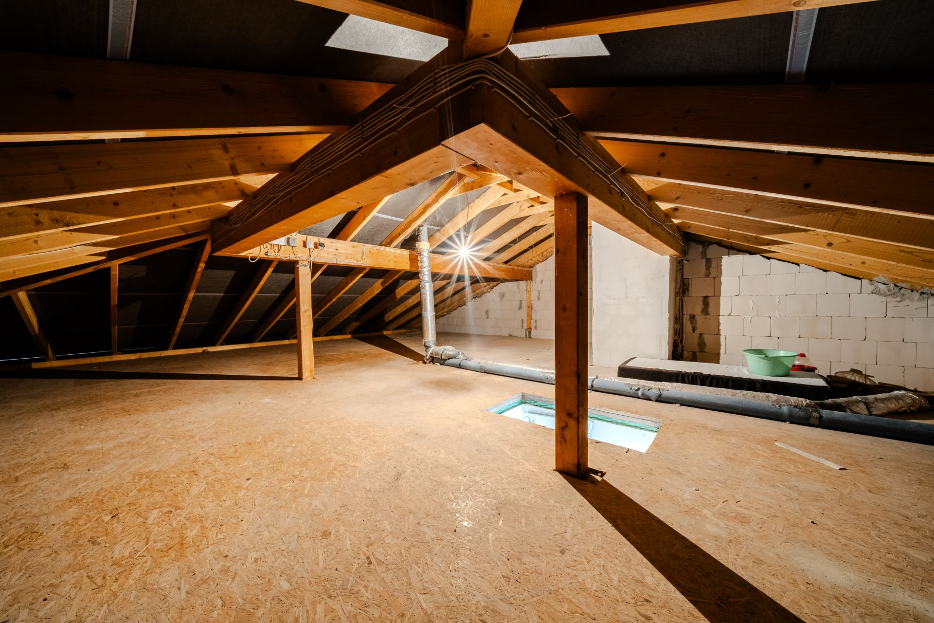 Dachbodenraum mit Holzbalken und OSB-Boden, Tageslicht fällt durch eine Öffnung ein.