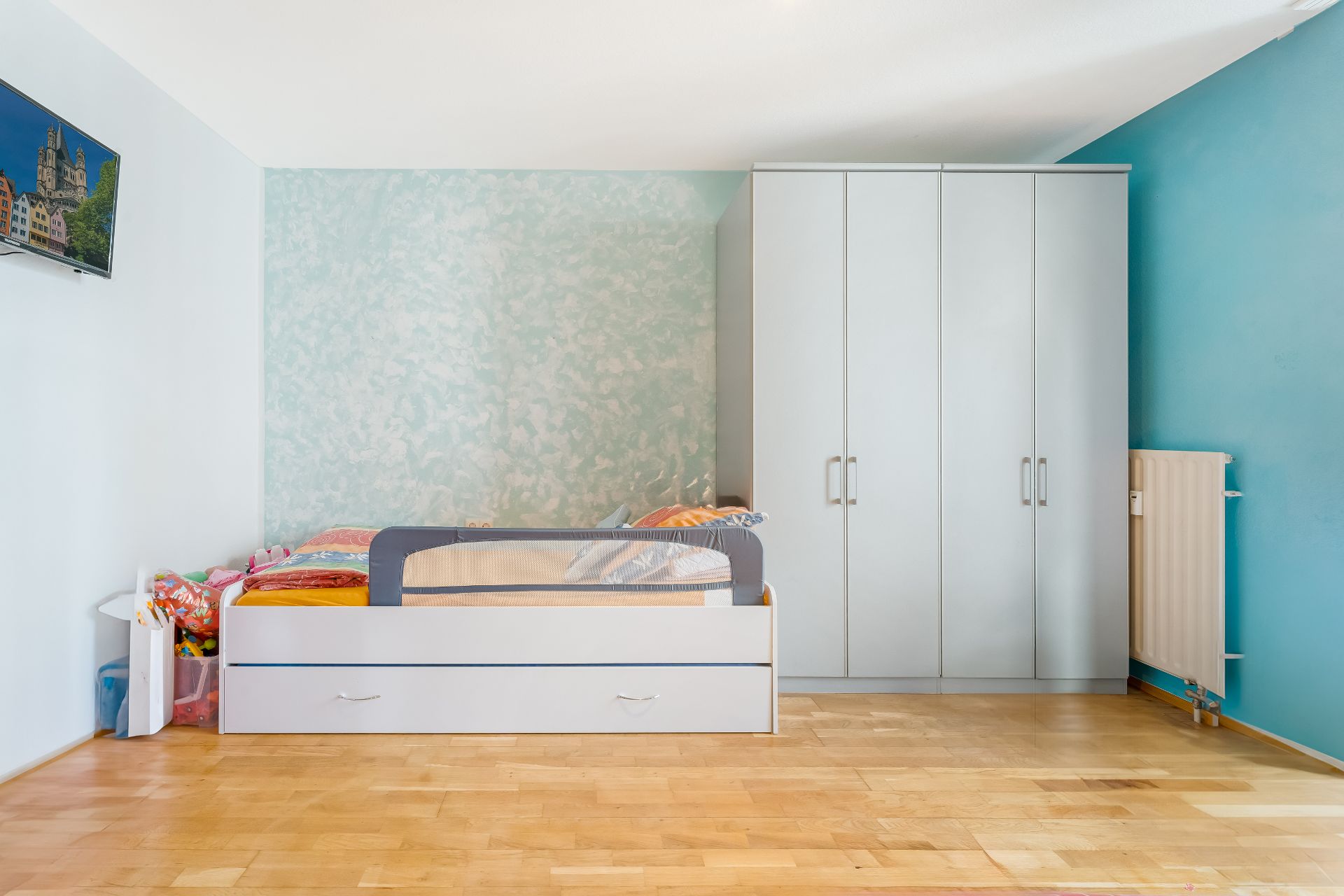 Helles Kinderzimmer mit Einzelbett, großem Kleiderschrank und Parkettboden.