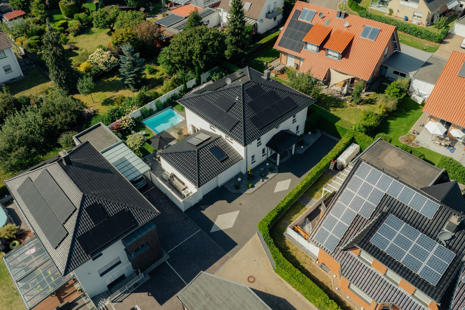 Luftaufnahme von Wohnhäusern mit Solaranlagen auf den Dächern und einem Garten mit Pool.