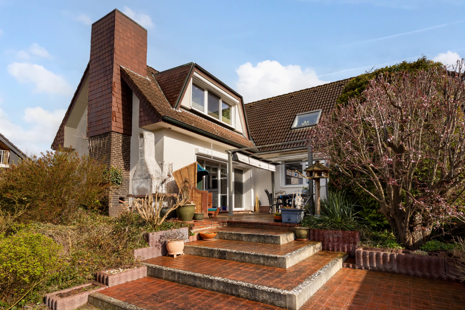 Einfamilienhaus mit Terrasse, Pflanzen und breiter Treppe im Garten.