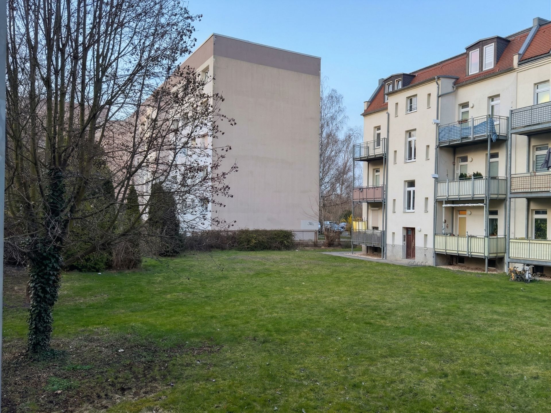 Grüne Rasenfläche mit Bäumen neben einem Mehrfamilienhaus mit Balkonen.