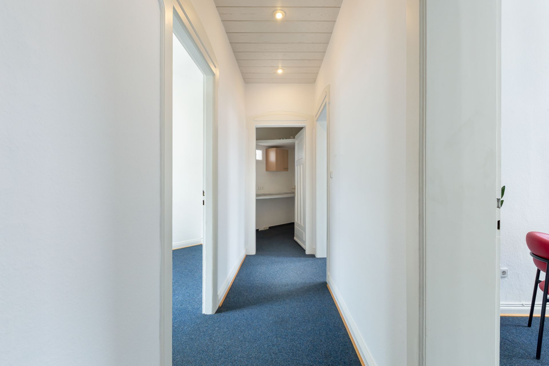 Heller Flur mit blauer Teppichboden und weißen Wänden, mehrere Türen führen zu anderen Räumen.