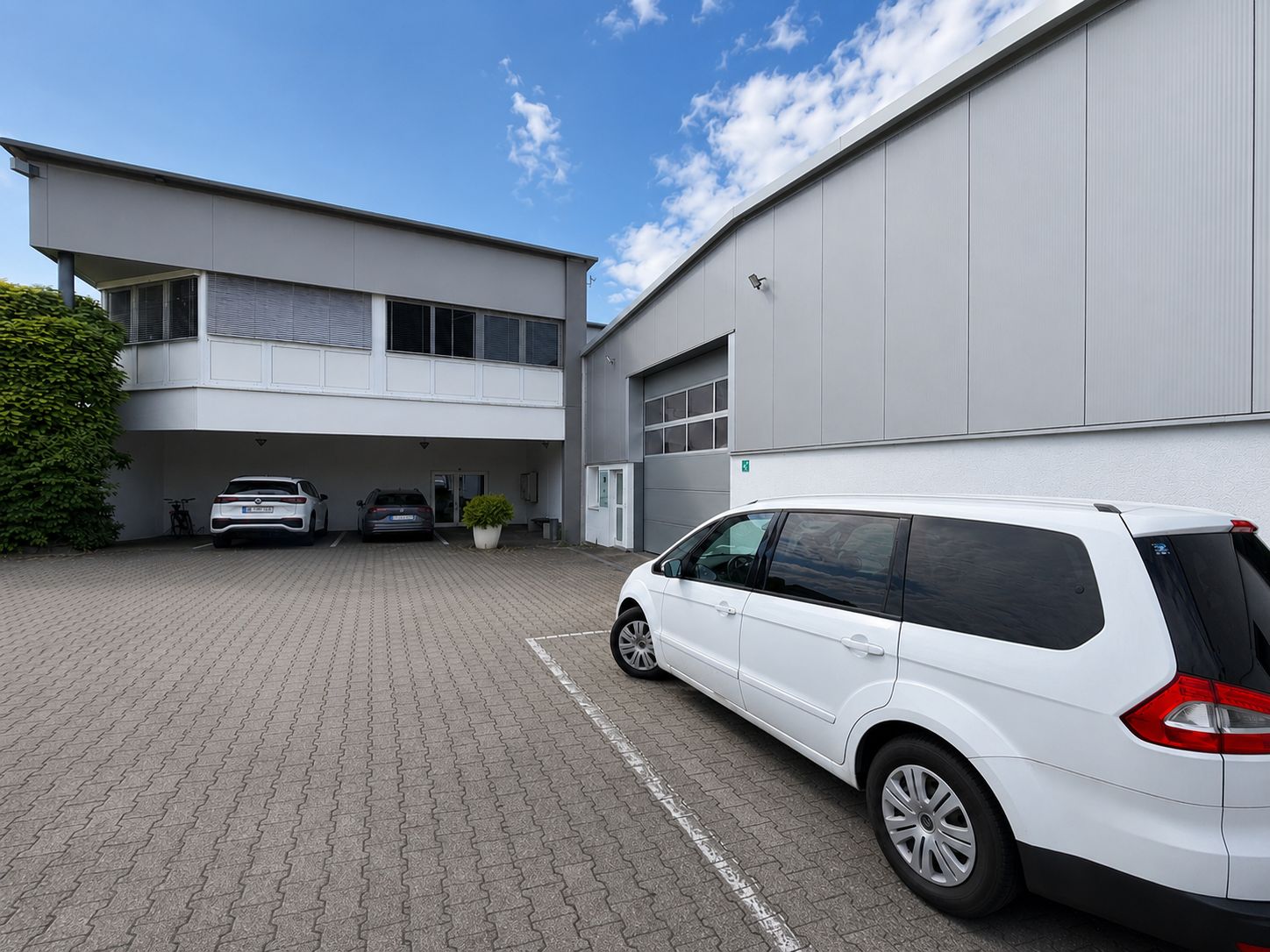 Gepflasterter Hof mit drei geparkten Autos neben einem modernen Gebäude bei Tageslicht.