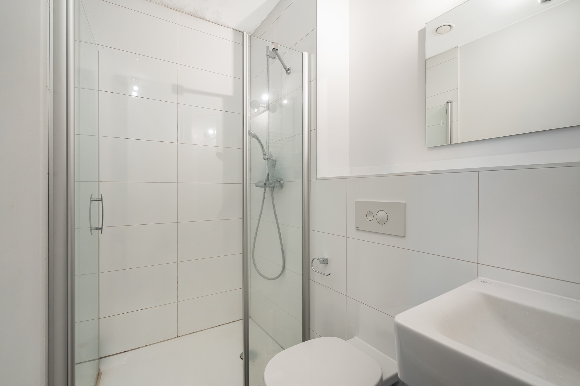 Modernes Badezimmer mit Dusche, Toilette, Waschbecken und Spiegel, alles in Weiß gehalten.