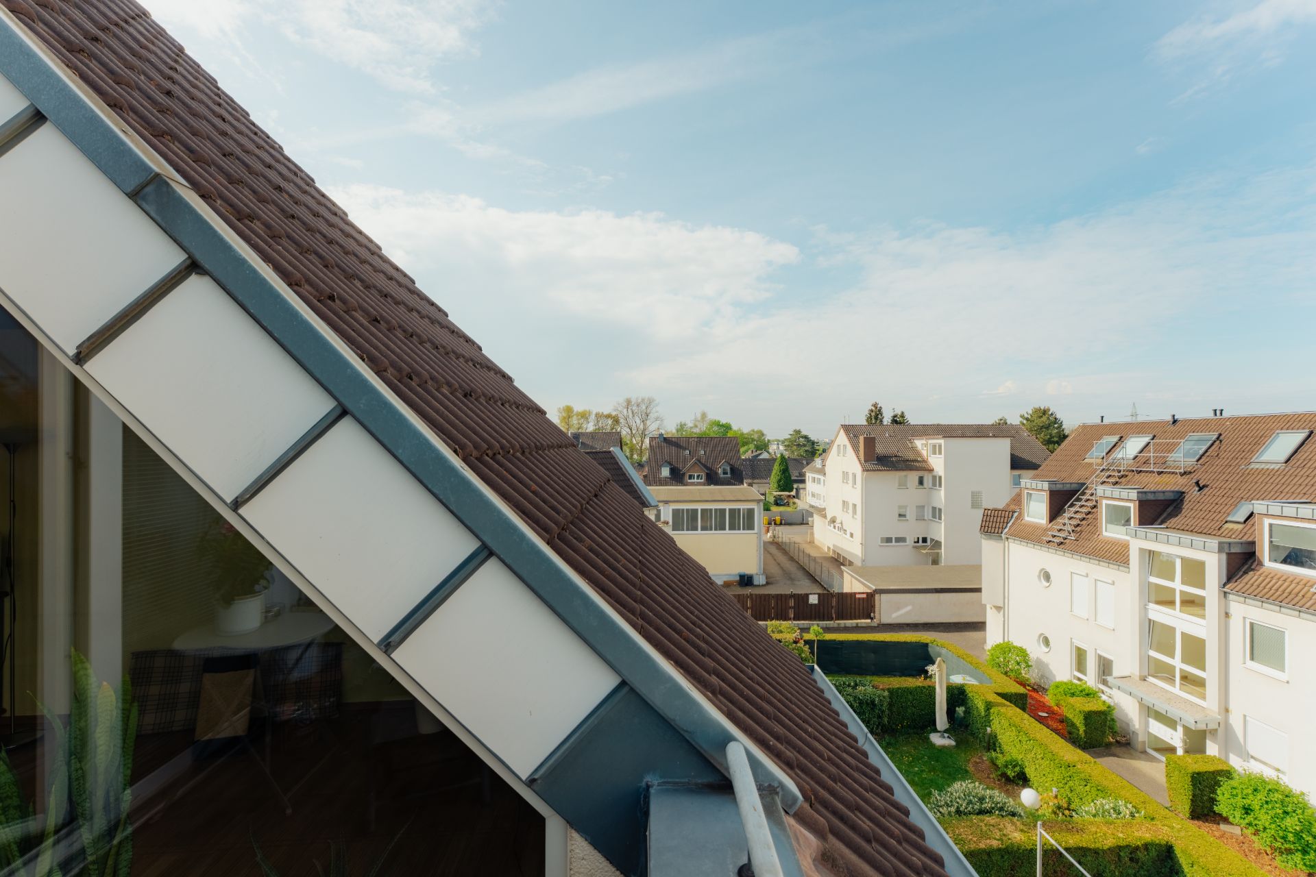 Blick von einem Balkon auf Wohnhäuser und gepflegte Gärten bei sonnigem Wetter.