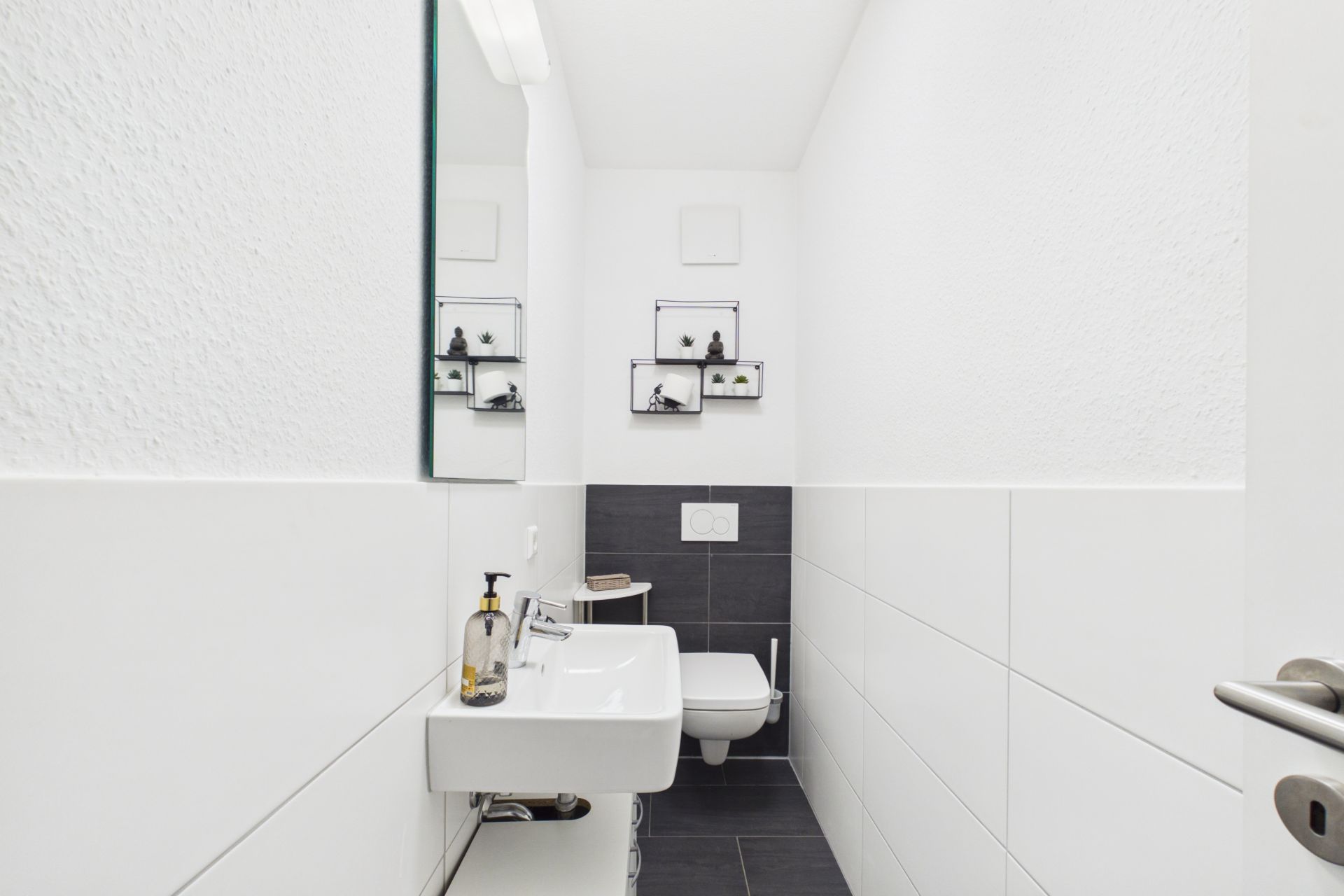Schmales, modernes Badezimmer mit Waschbecken, Spiegel und wandhängender Toilette.