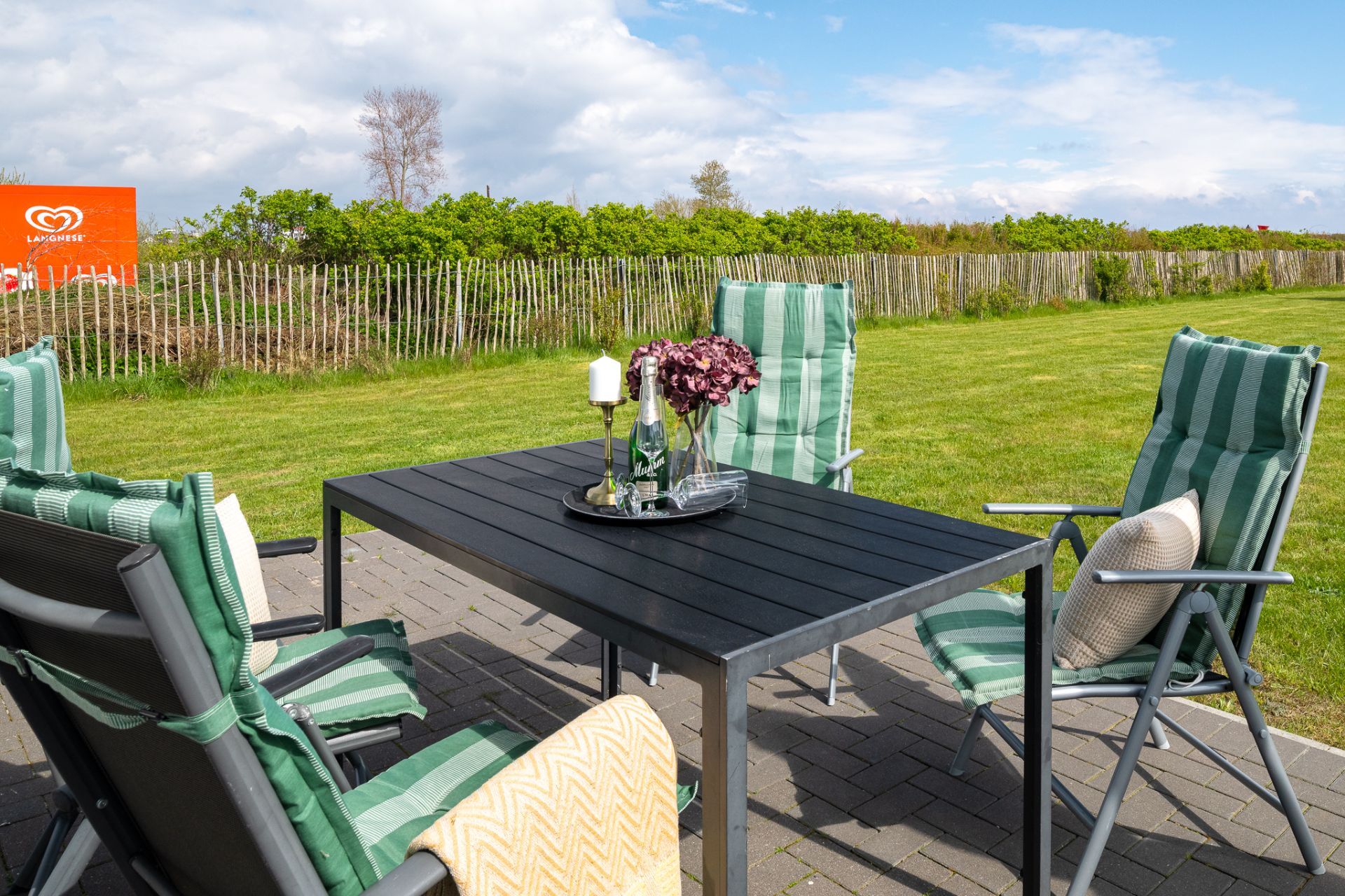 Gartentisch mit vier gepolsterten Stühlen auf einer Terrasse vor Rasen.