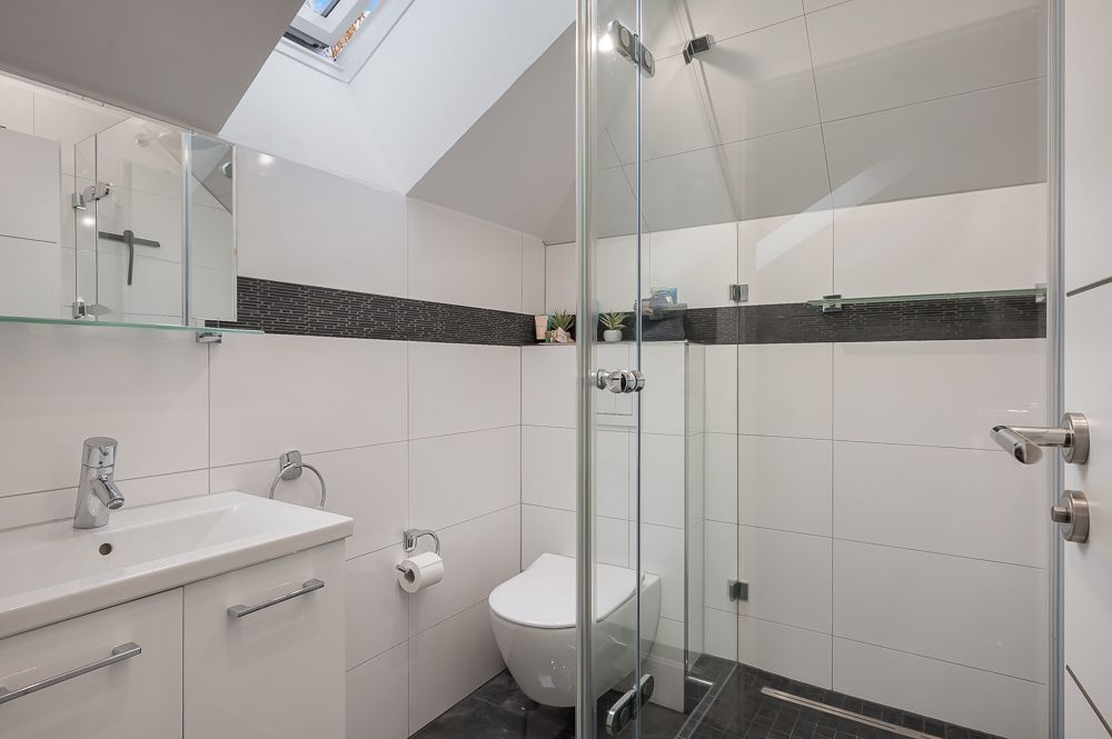 Modernes Badezimmer mit Dusche, WC, Waschbecken und Dachfenster.
