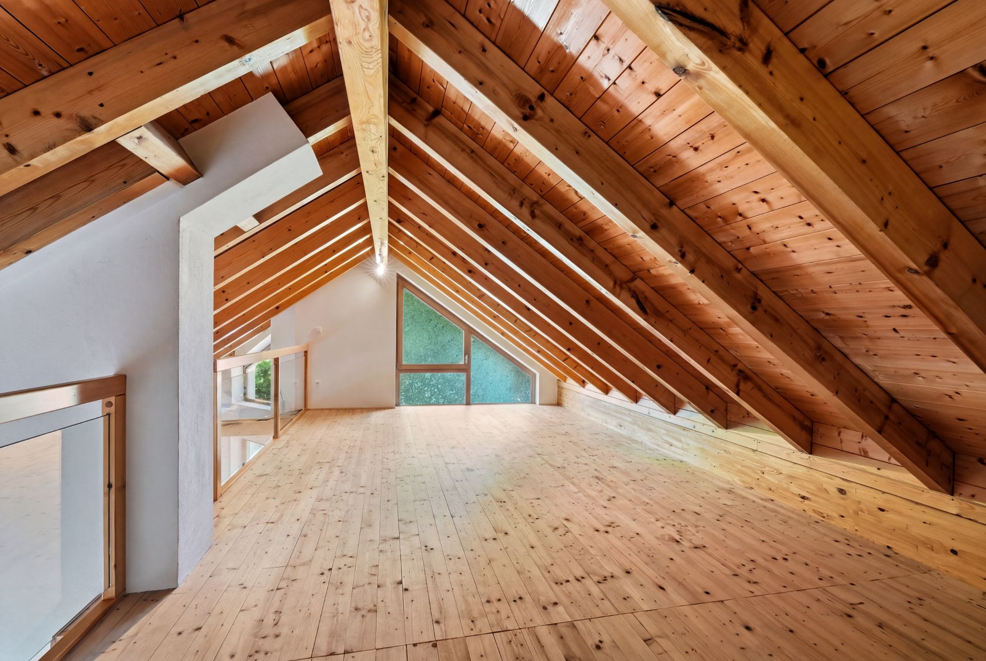 Dachgeschossraum mit Holzdecke, Holzboden und großem Fenster am Giebel.