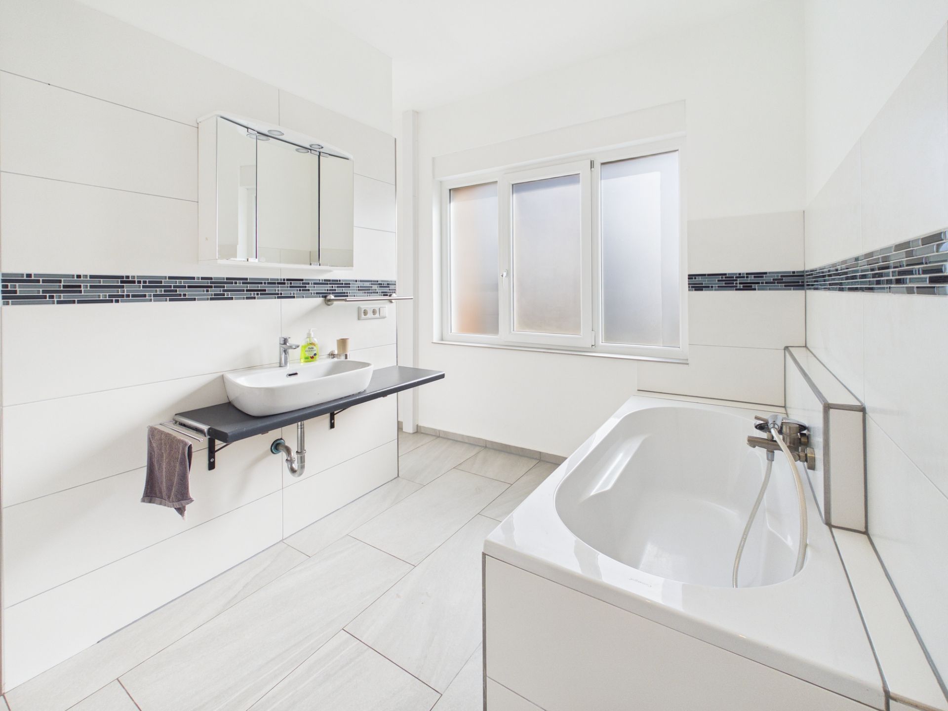 Modernes Badezimmer mit Badewanne, Waschbecken und großem Fenster.