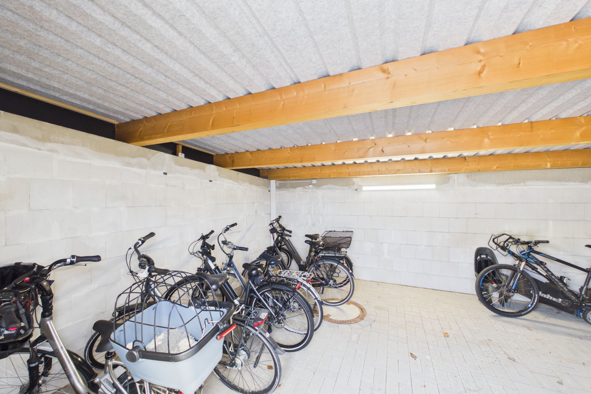 Überdachter Abstellraum mit mehreren abgestellten Fahrrädern auf hellem Boden.