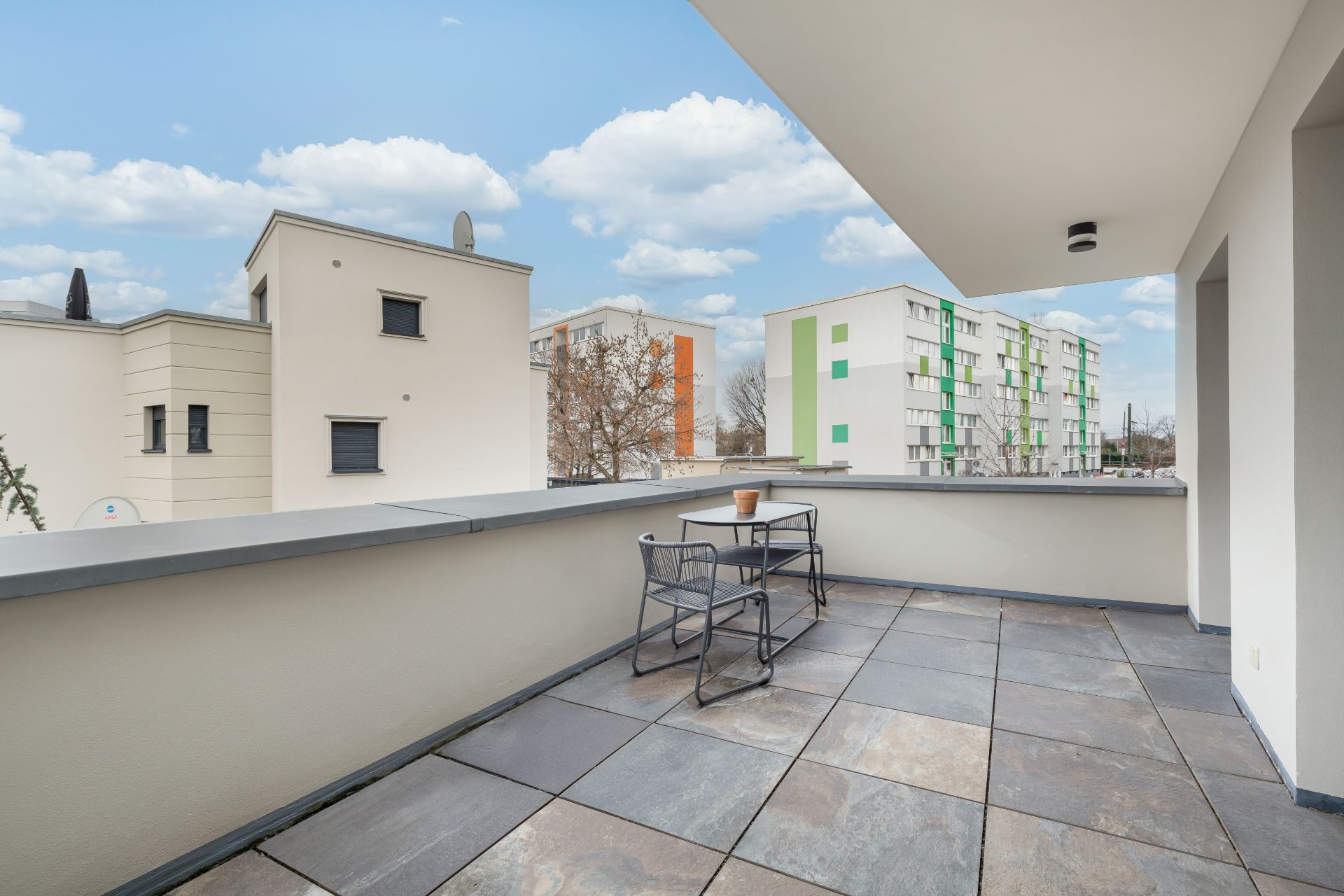 Großer Balkon mit Tisch und zwei Stühlen, Blick auf Wohngebäude bei Tageslicht.