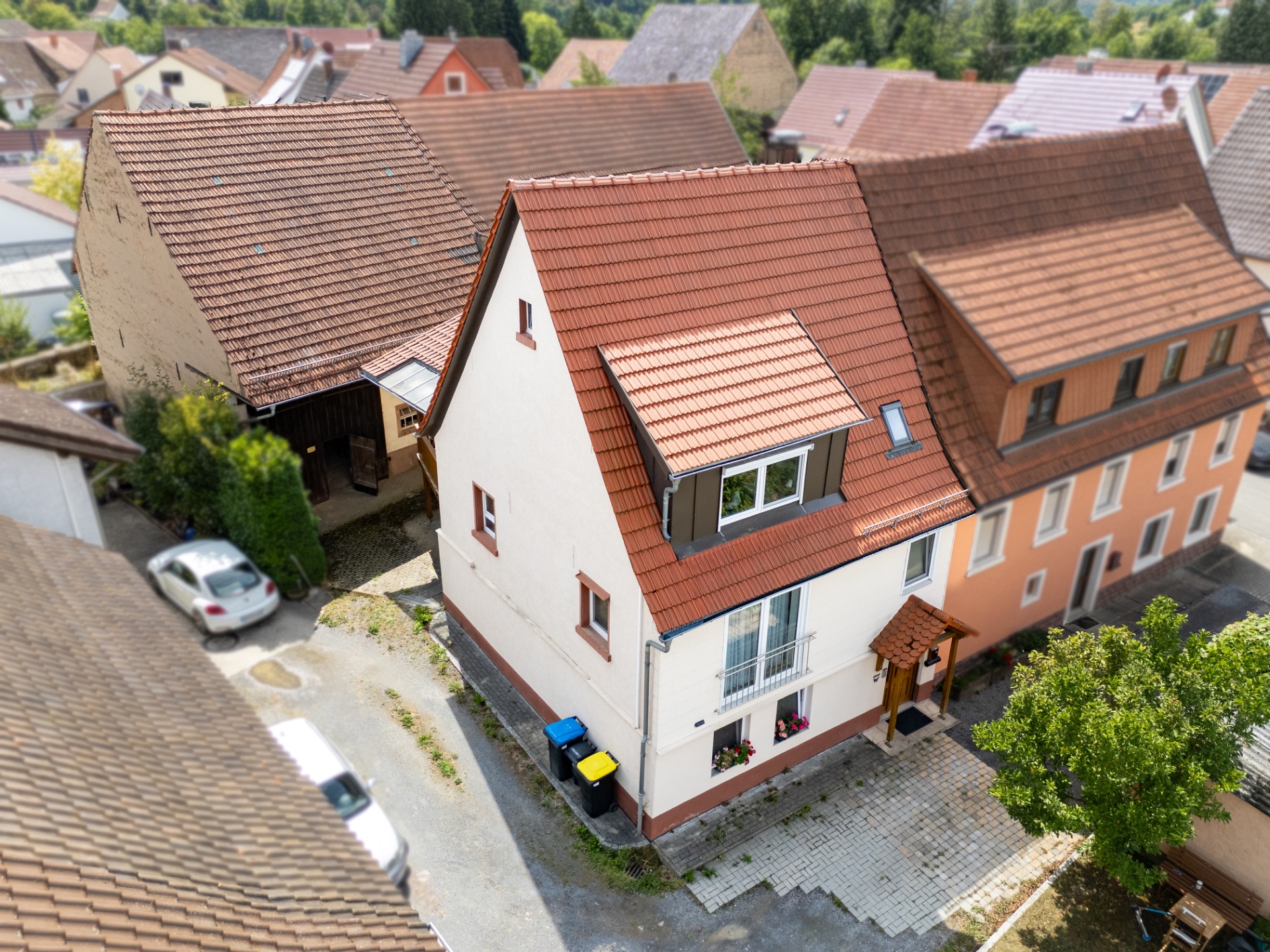 Drohnenaufnahme eines freistehenden Hauses mit rotem Dach und Vorgarten in einer Wohngegend.