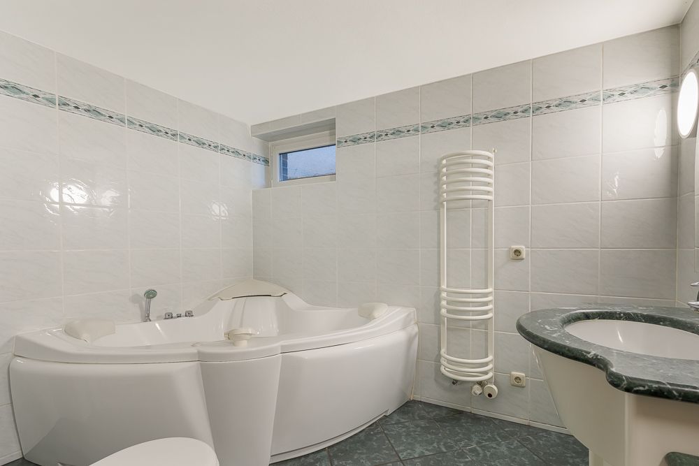 Modernes Badezimmer mit Eckbadewanne, Waschbecken, Heizung und kleinem Fenster.