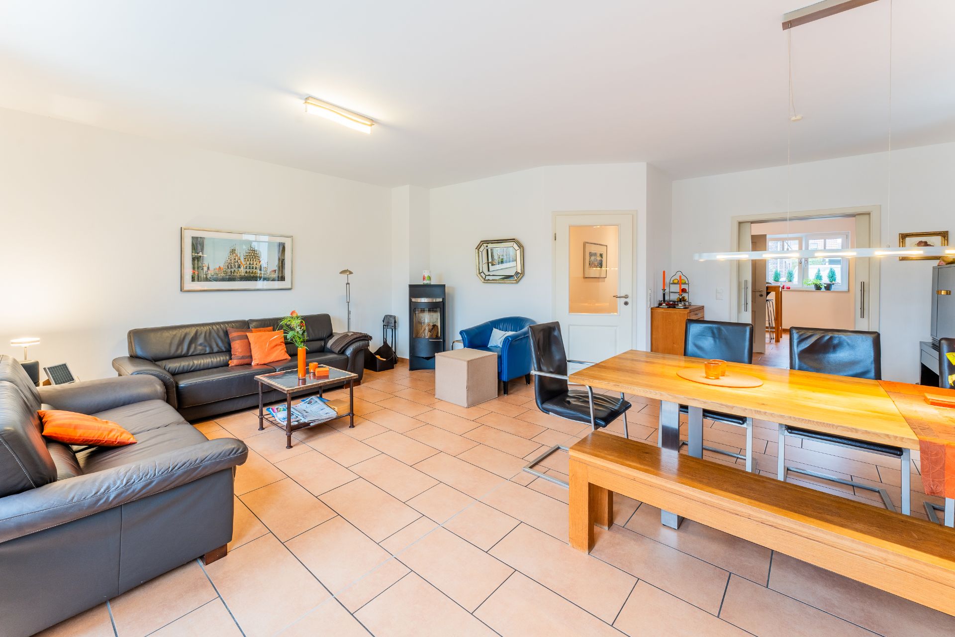 Helles Wohnzimmer mit Ledersofas, Esstisch, Holzbank und Fliesenboden.