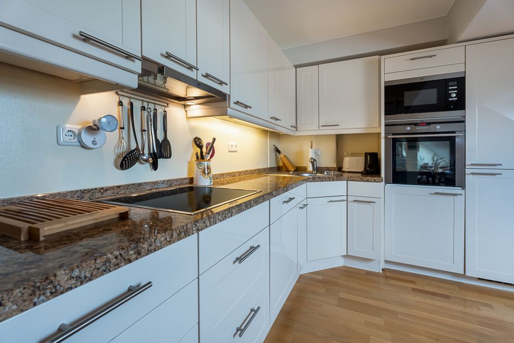 Moderne Einbauküche mit weißen Schränken, Kochfeld, Backofen und Küchenutensilien an der Wand.
