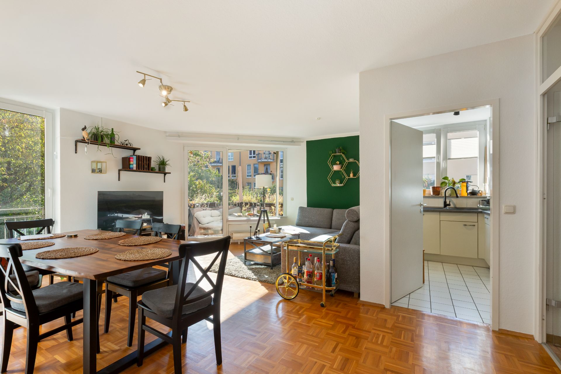 Helles Wohnzimmer mit Essbereich, Sofa, Regal und Zugang zur offenen Küche.