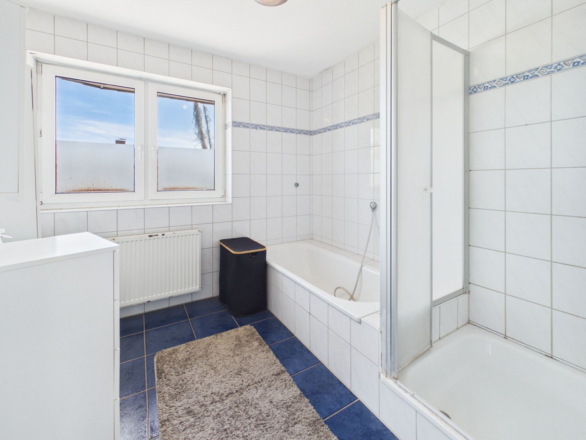 Modernes Badezimmer mit Badewanne, Dusche, Fenster und blauen Fliesen.