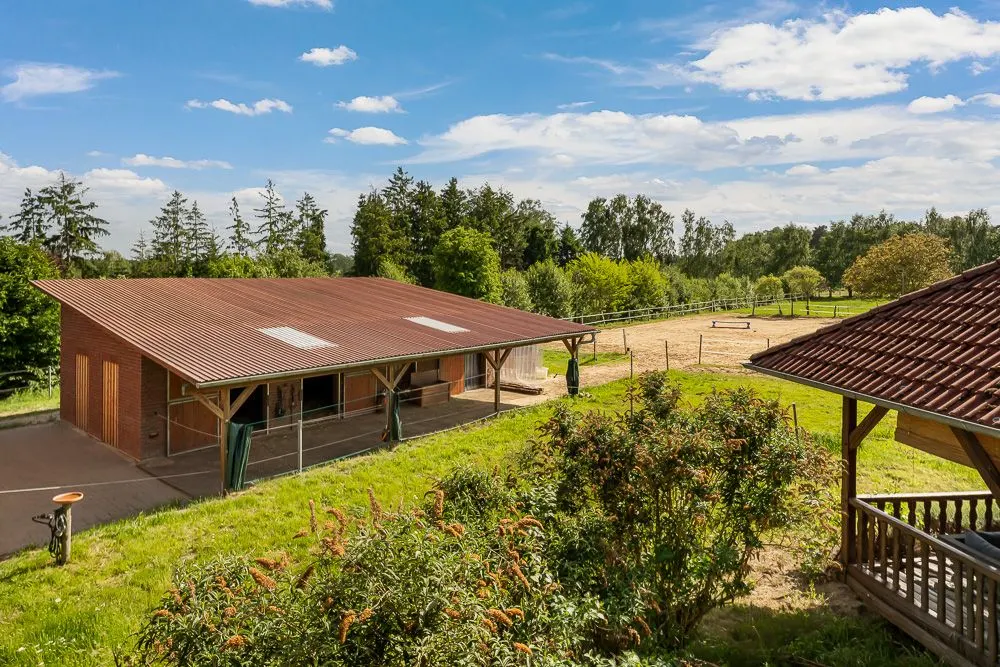 Stallgebäude mit Auslauf und angrenzender Weide, umgeben von Bäumen und Sträuchern.