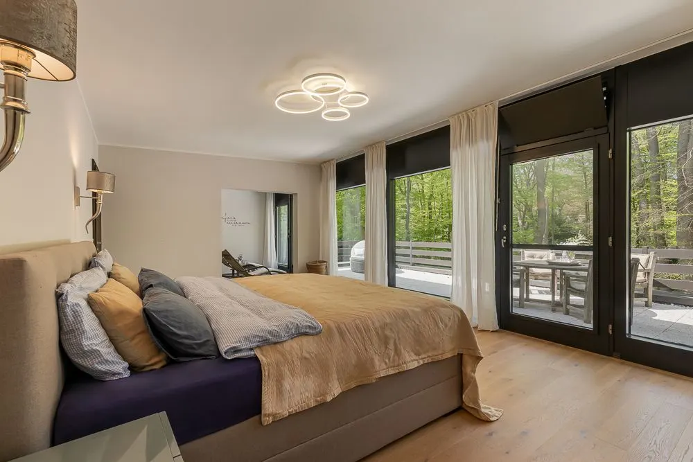 Modernes Schlafzimmer mit großem Bett und Zugang zu einer Terrasse mit Blick auf Bäume.