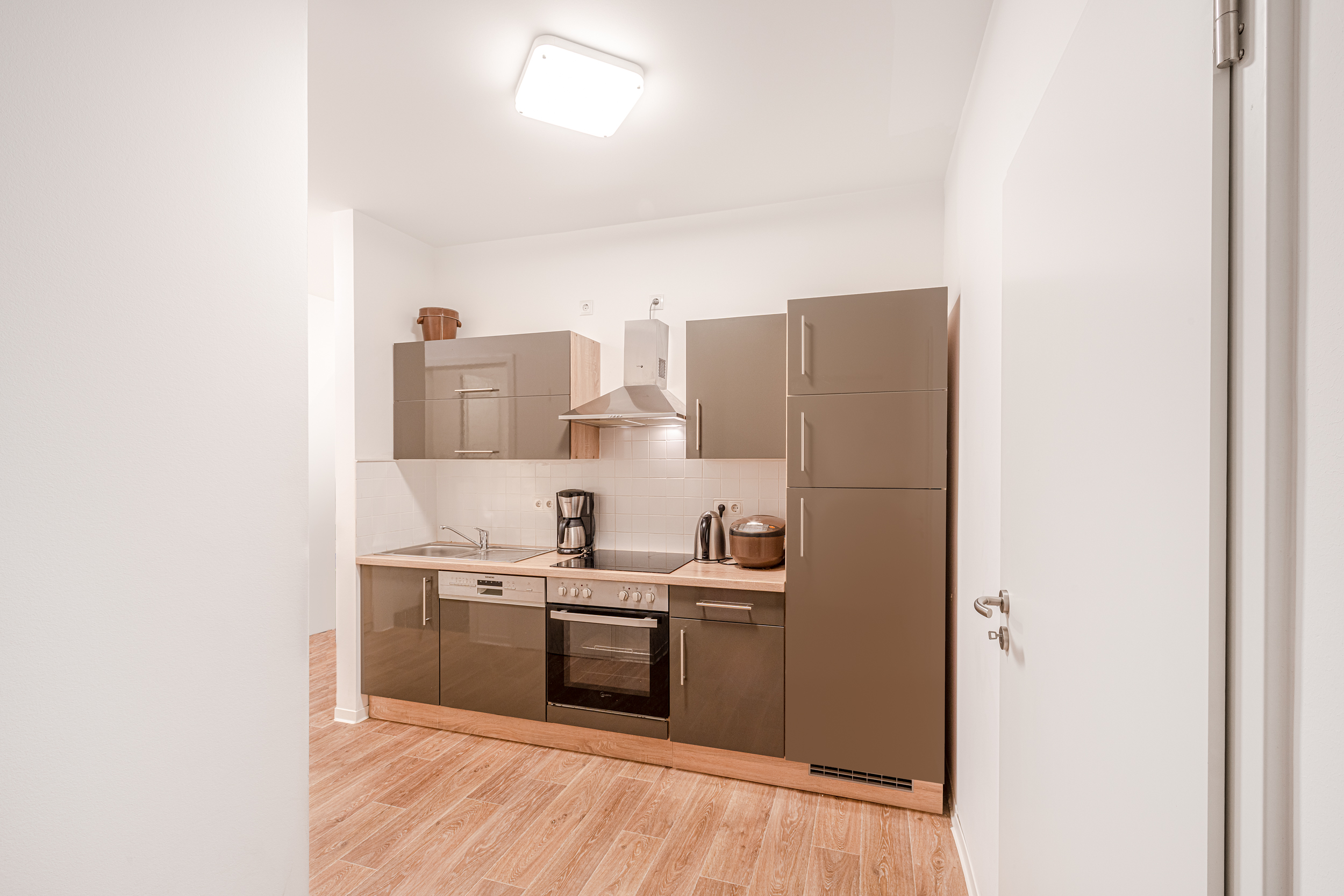 Moderne Einbauküche mit Herd, Spüle, Kaffeemaschine und hellen Holzboden.