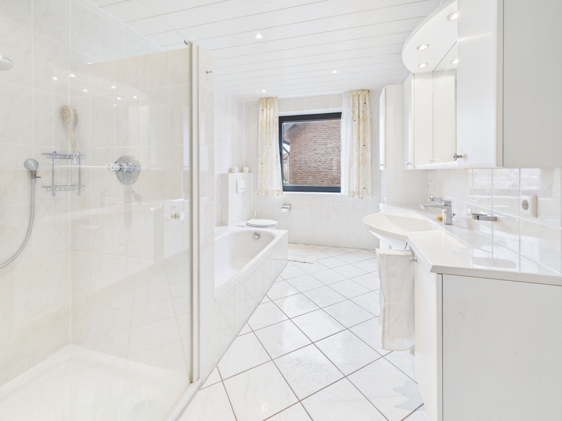 Helles Badezimmer mit Dusche, Badewanne, großem Fenster und weißen Fliesen.