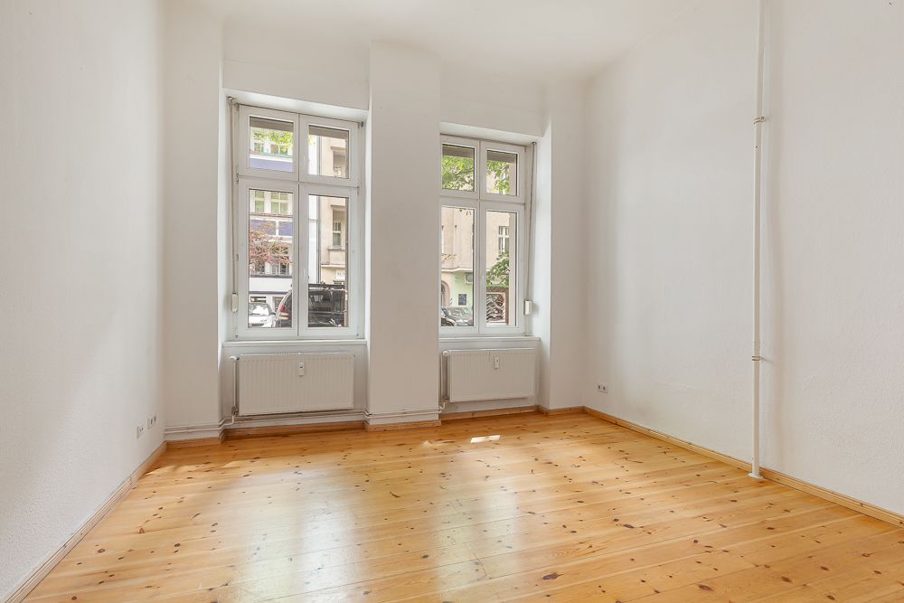 Leerer Raum mit Holzfußboden und zwei großen Fenstern mit Blick nach draußen.