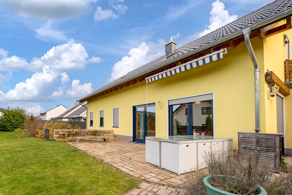 Gelbes Wohnhaus mit Terrasse, Markise und Garten an einem sonnigen Tag.