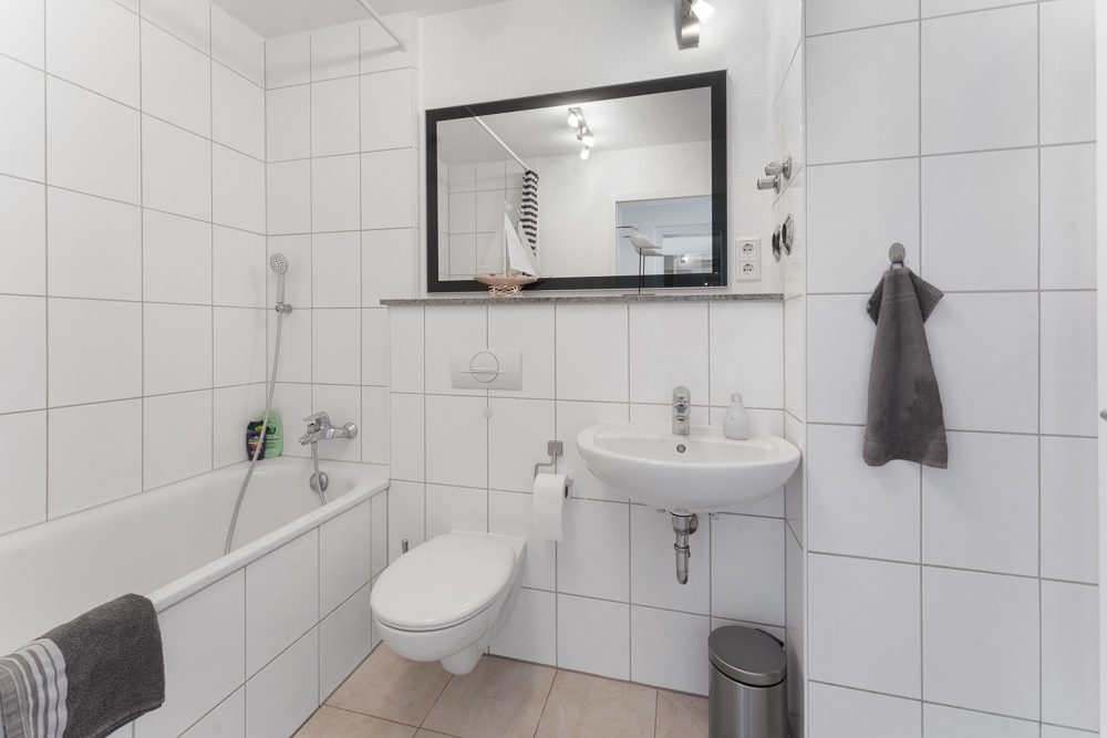 Modernes Badezimmer mit Badewanne, Wandtoilette, Waschbecken und großem Spiegel.