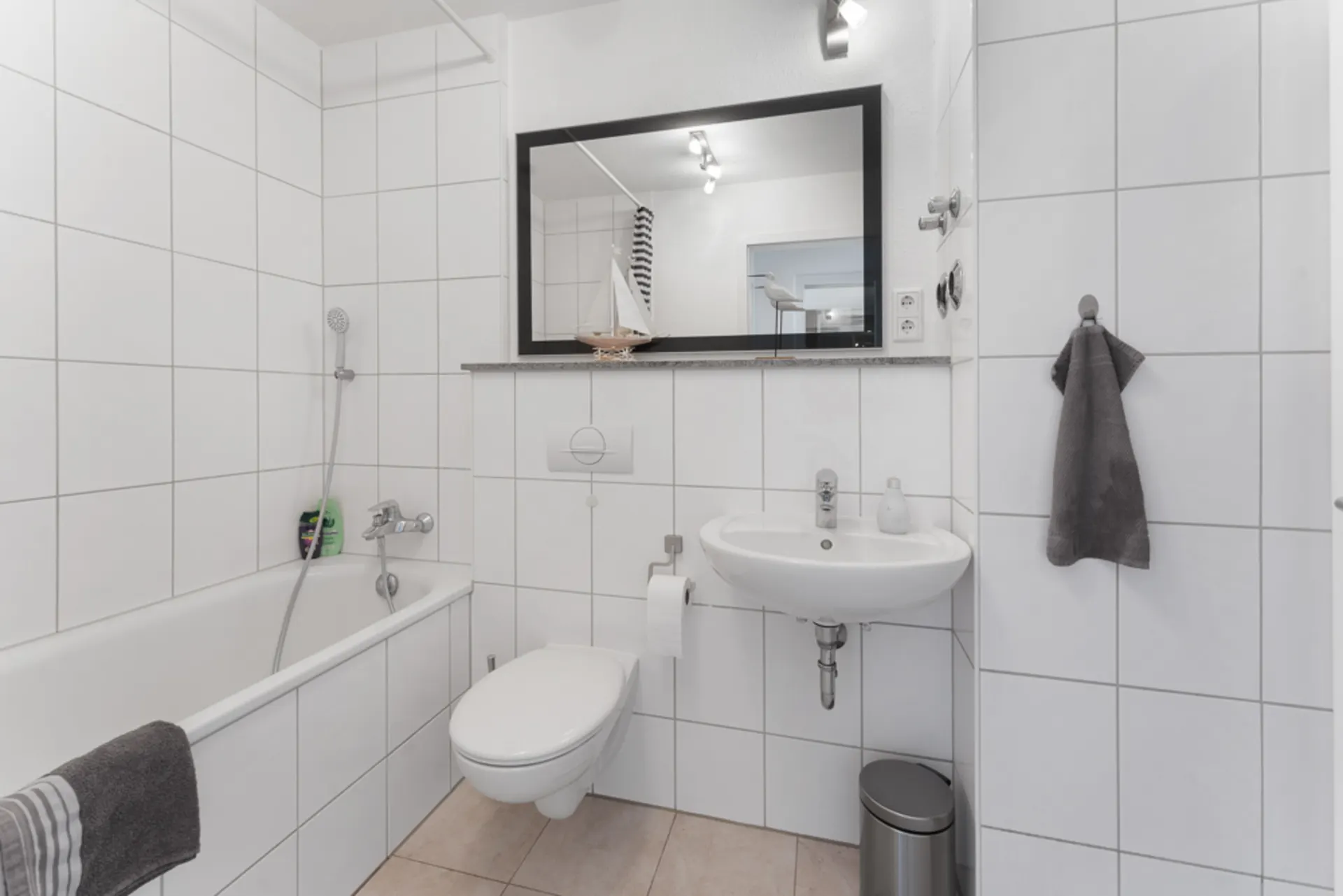 Modernes Badezimmer mit Badewanne, Wandtoilette, Waschbecken und großem Spiegel.
