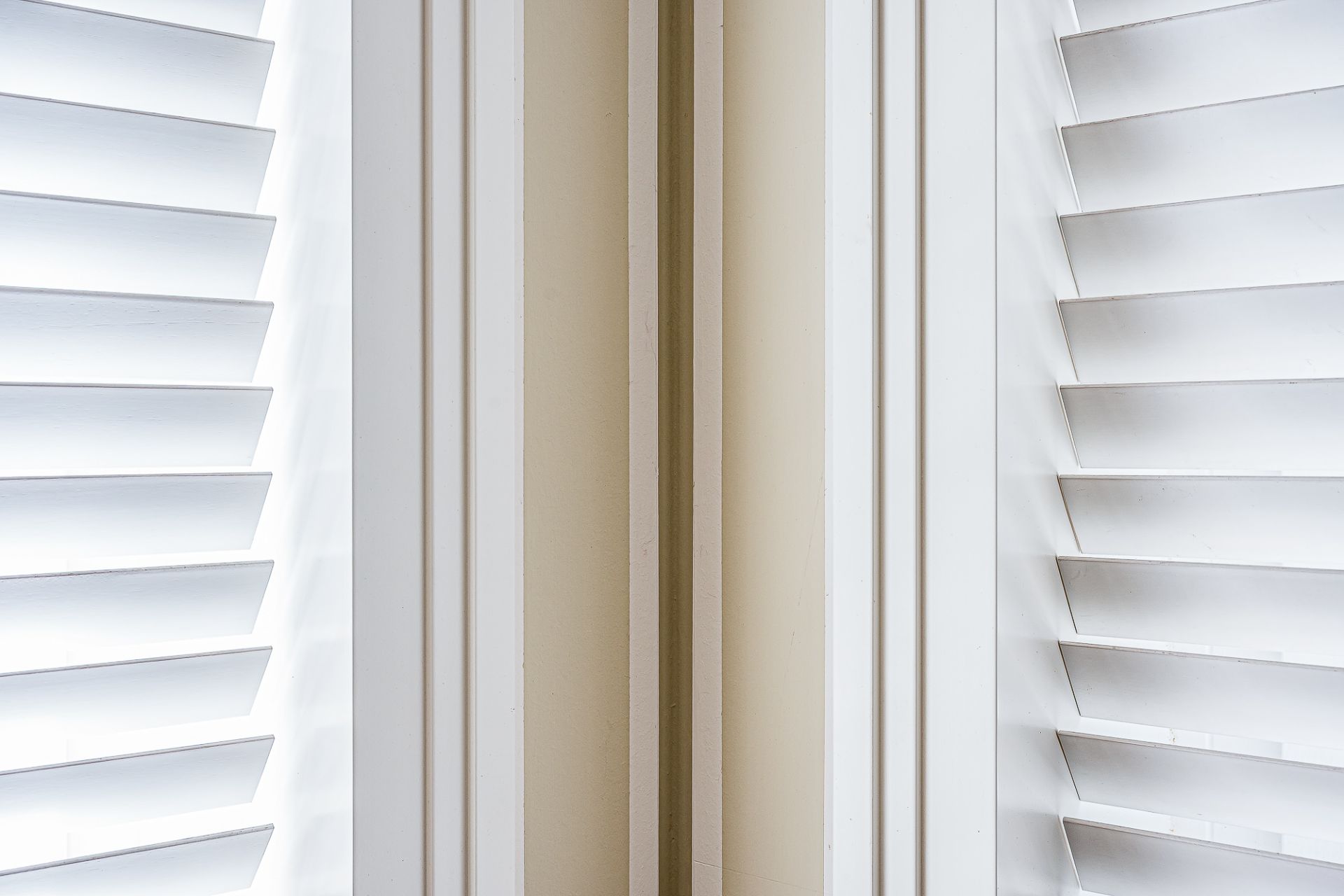Zwei weiße Fensterläden mit Lamellen an einer Raumecke.